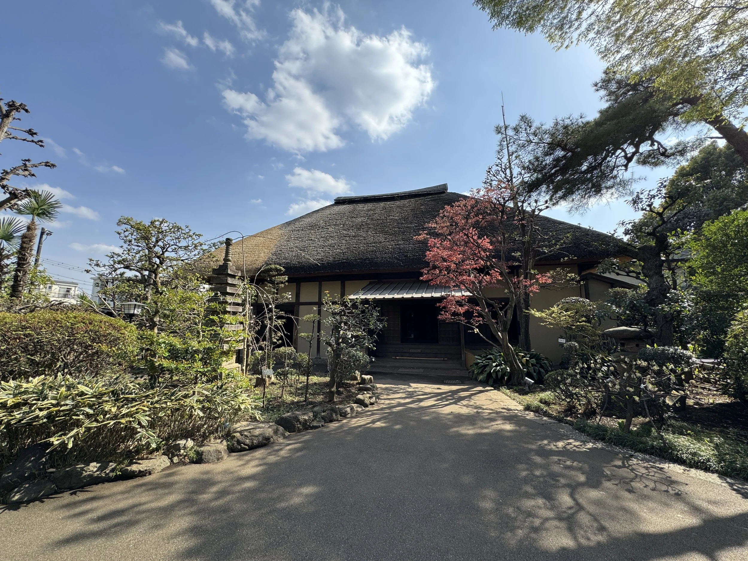 A traditional Japanese house with a thatched roof surrounded by trees and a garden.