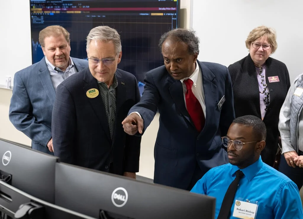 Man pointing to a computer screen as others look on in the First National Bank Alaska Finance lab.