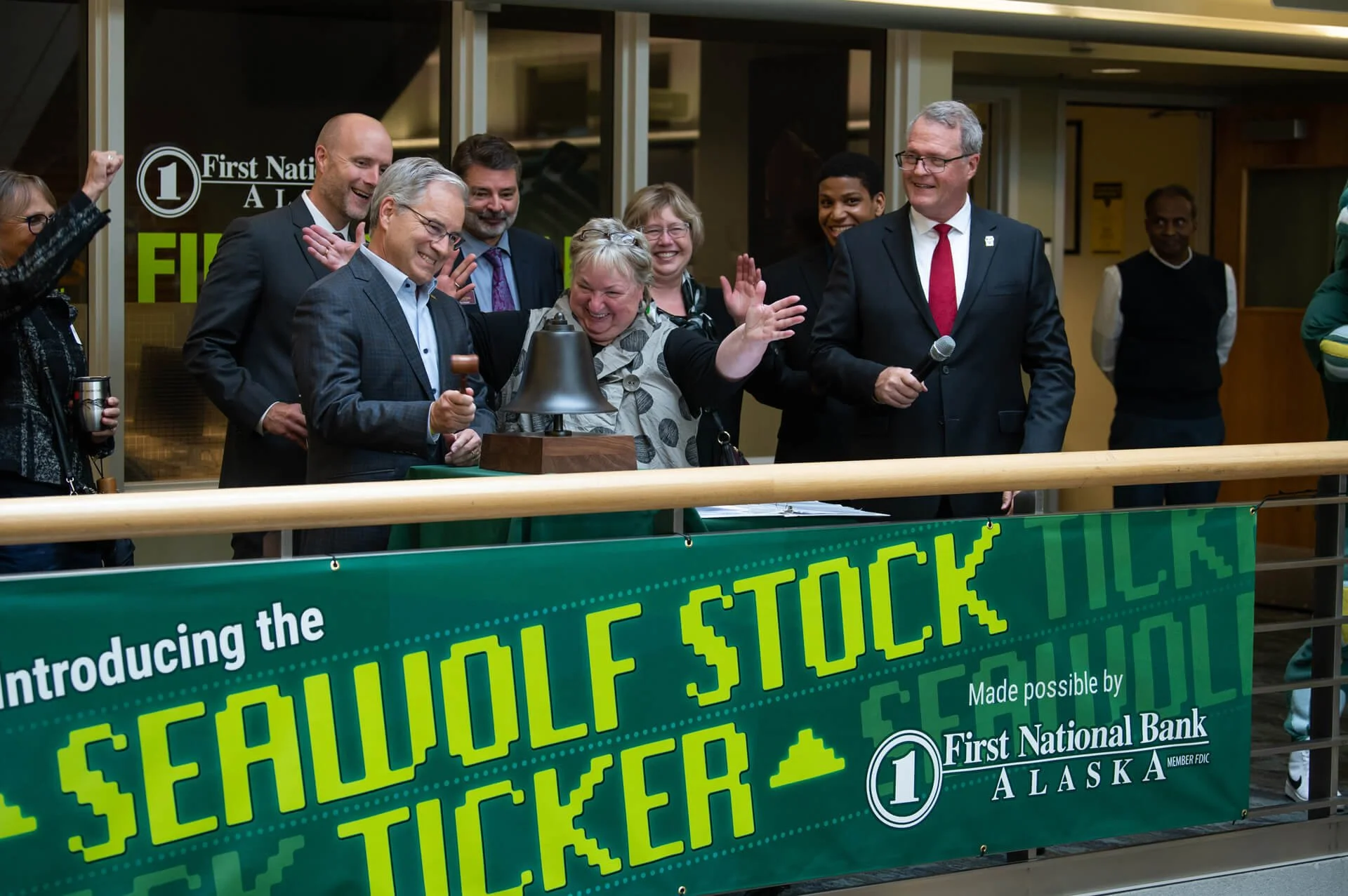 UAA Chancellor Sean Parnell and others ring a bell. Seawolf Stock Ticker banner in foreground.