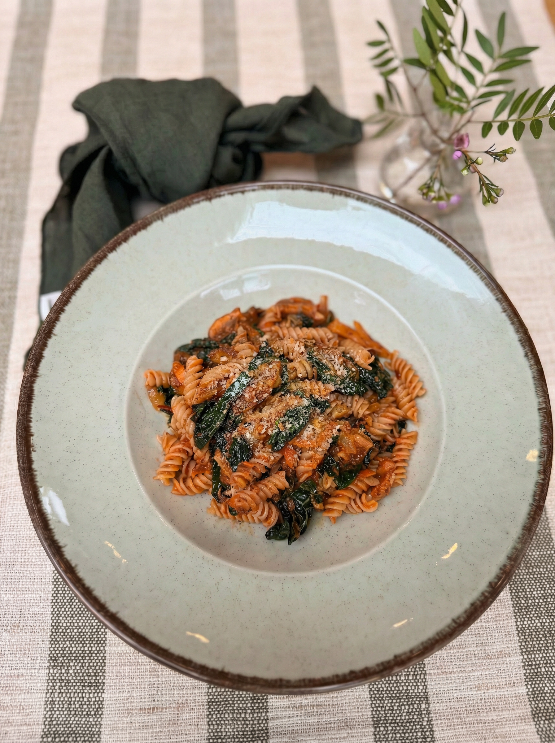 A green bowl of pasta on a green and cream striped table cloth