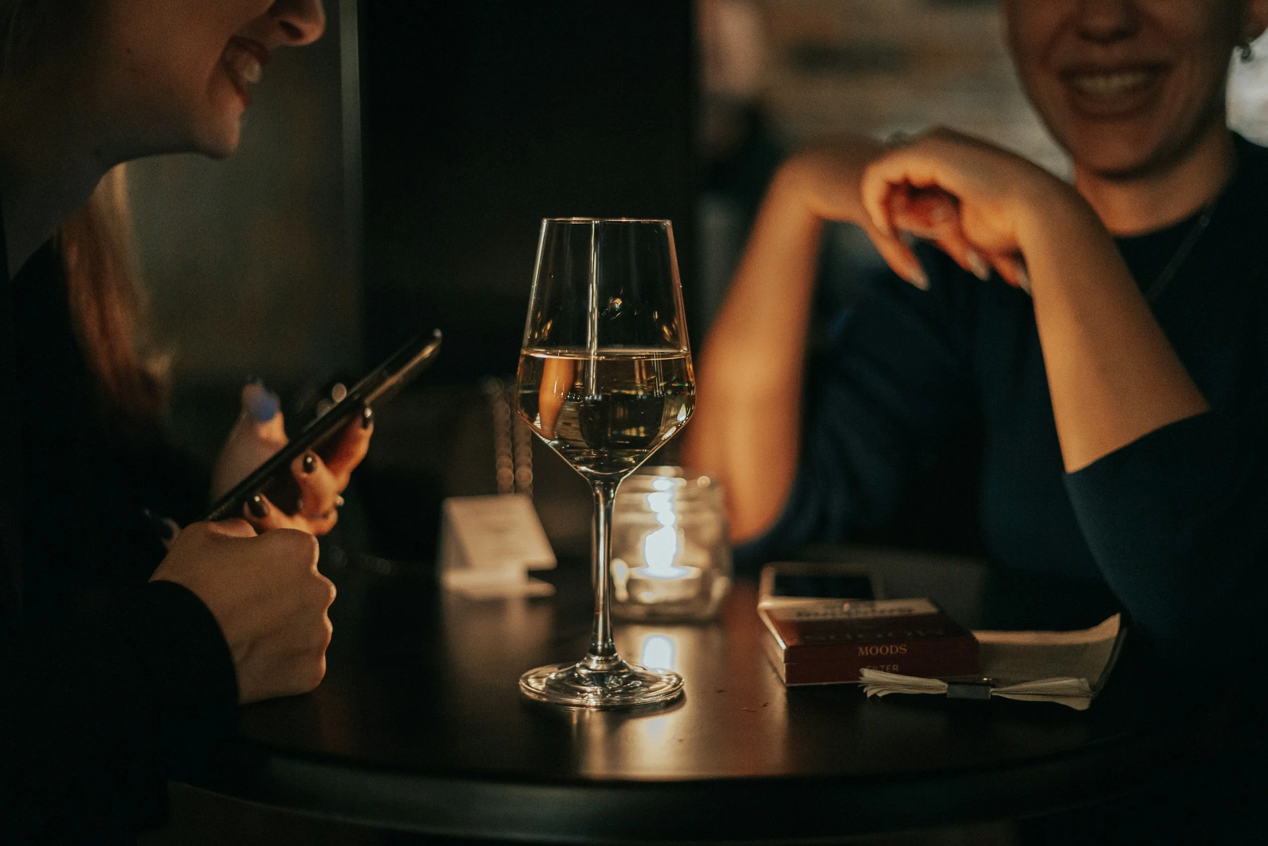 Two women laugh either side of a glass of wine  during an evenign out