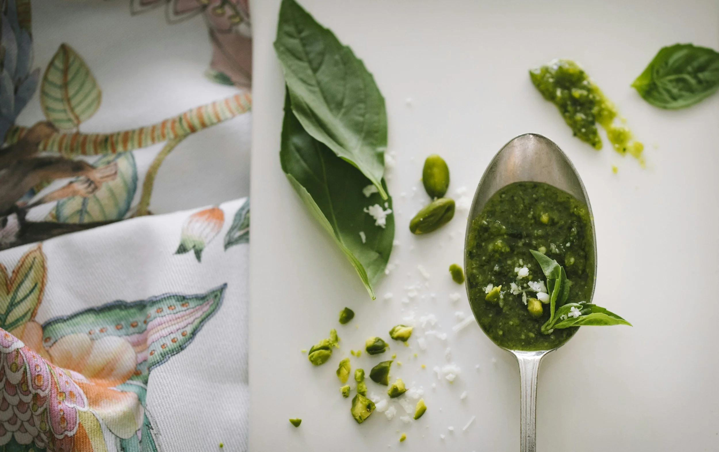 a spoon of pesto on a white background with some basil and salt beside it