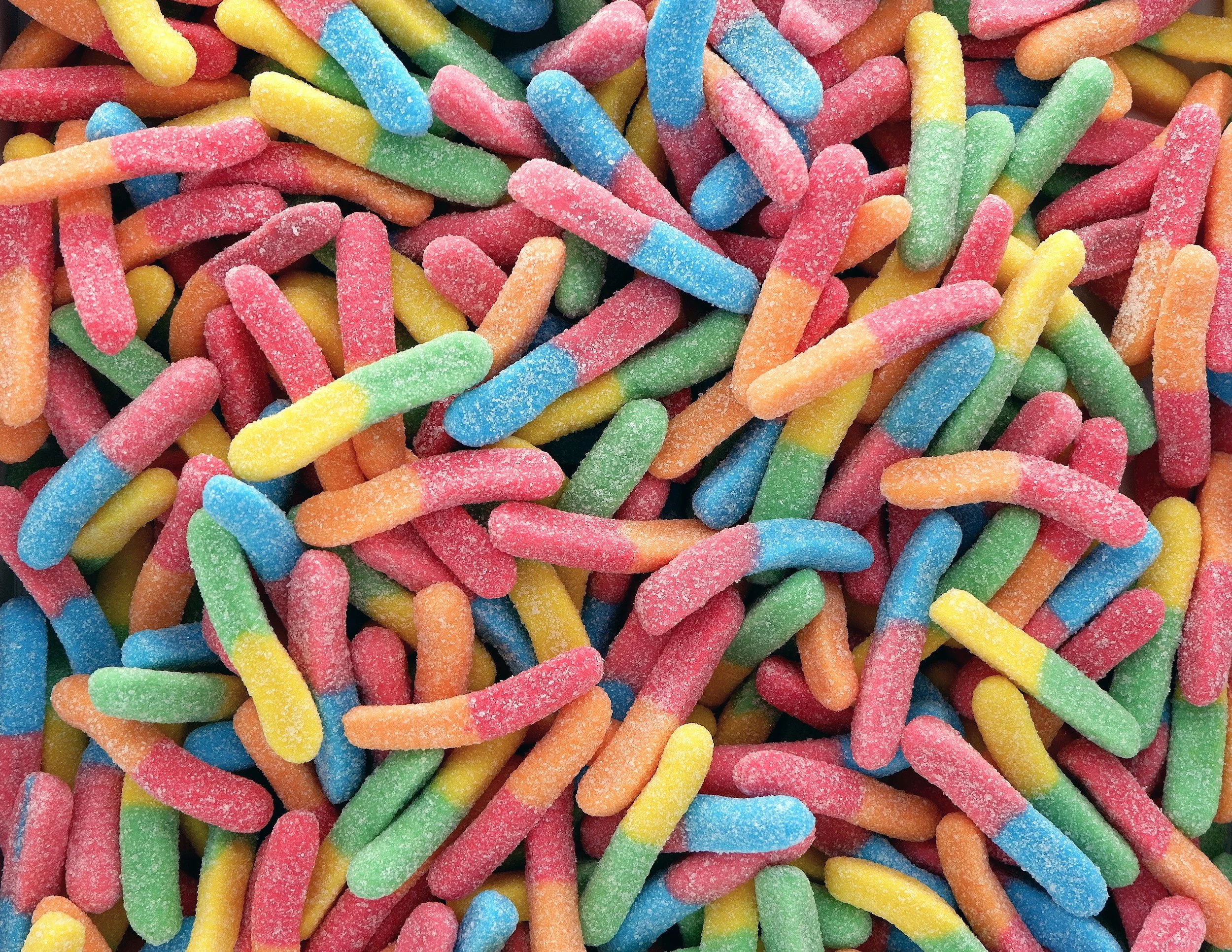 Close-up of colorful sour gummy worms resembling worms with multicolored sugar coating.