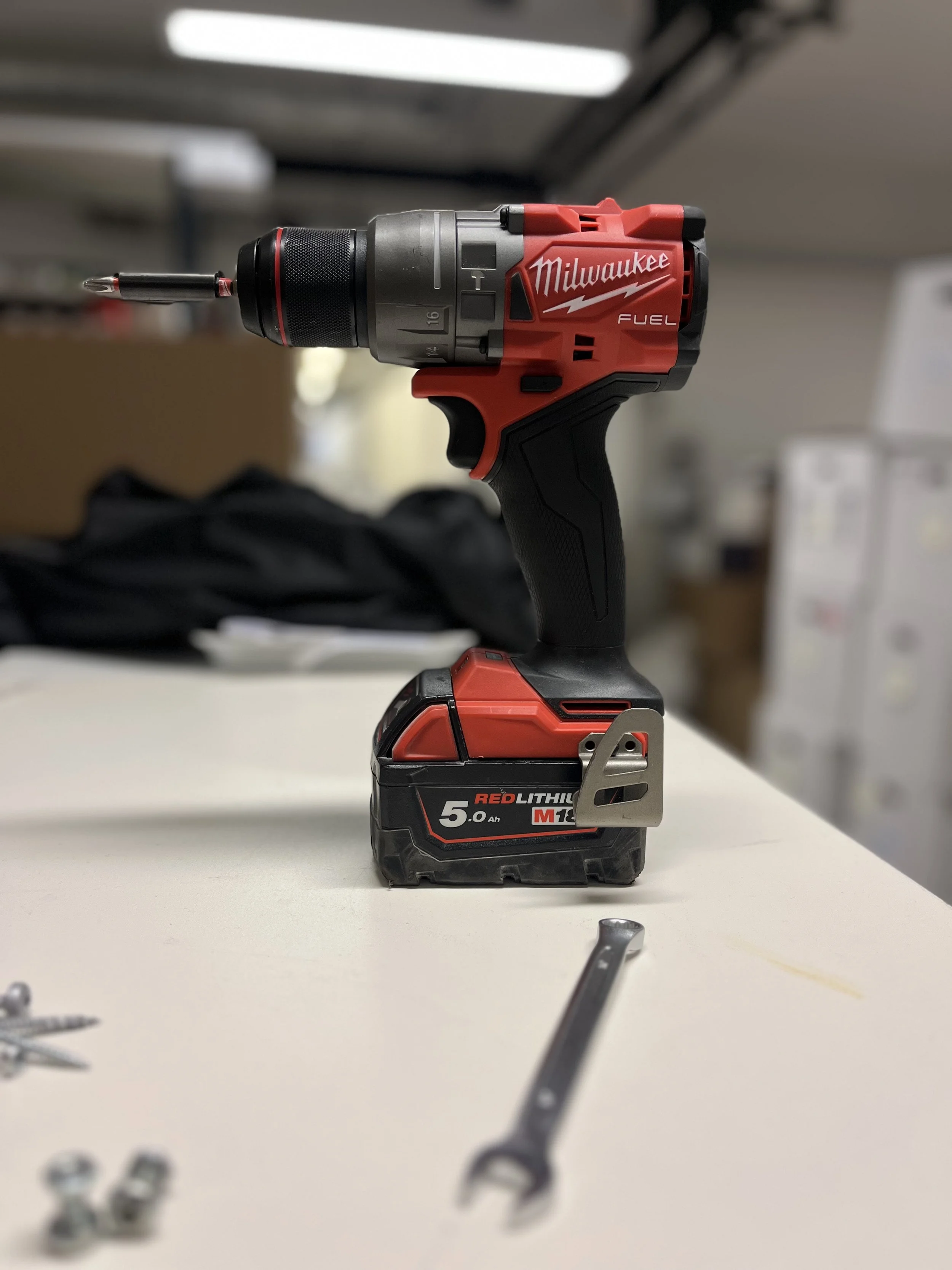 En rød og sort Milwaukee batteridrevet boremaskine med en 5.0 Ah batteripakke, placeret på et hvidt bord.