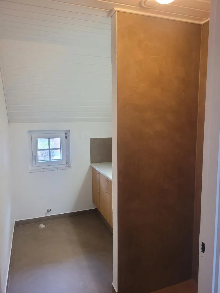 Et lille værelse med et vindue, et kabinet med skabsdøre, og en skillevæg lavet af træ.