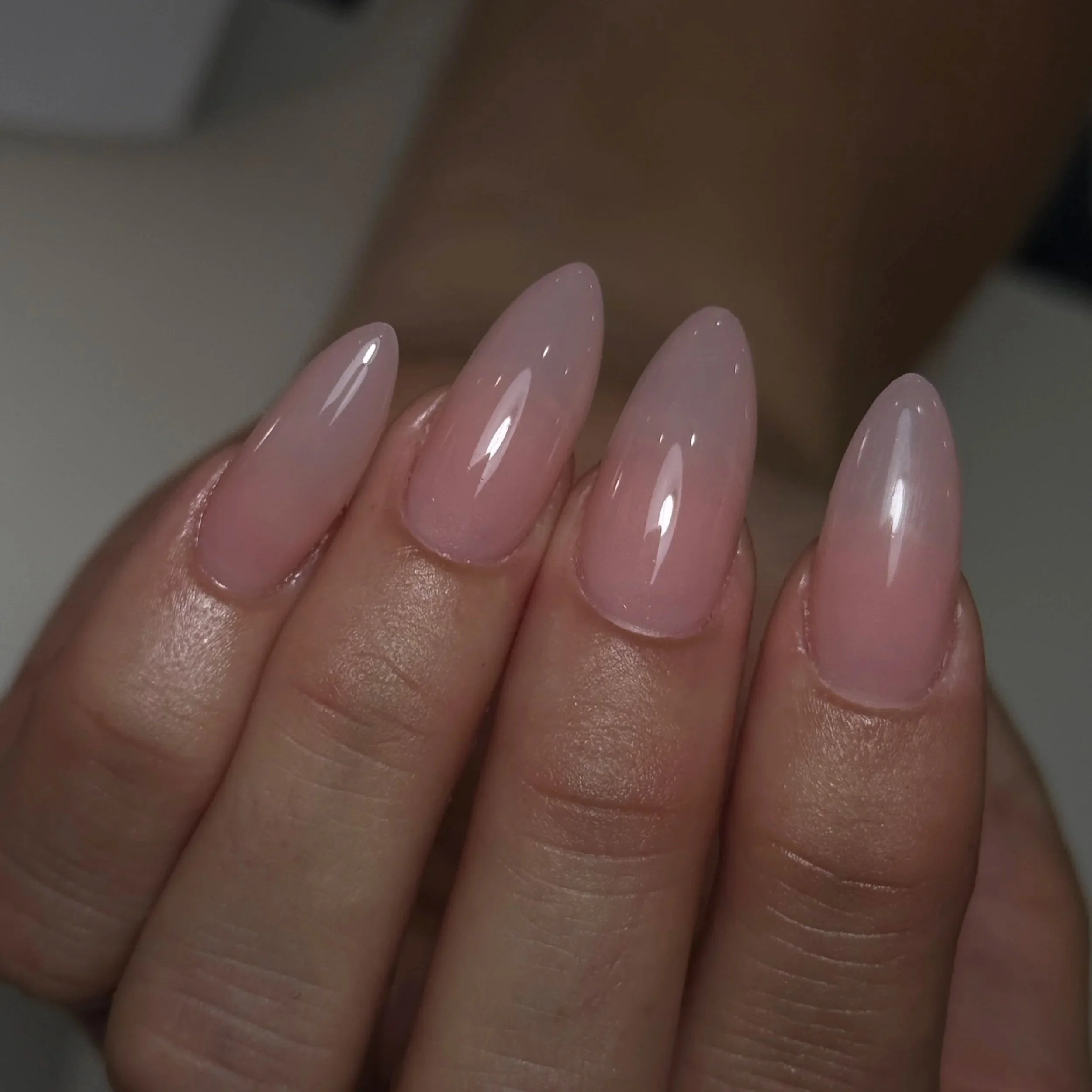 Close-up of a hand with manicured nails painted in a light pink color, with shiny, smooth surface.