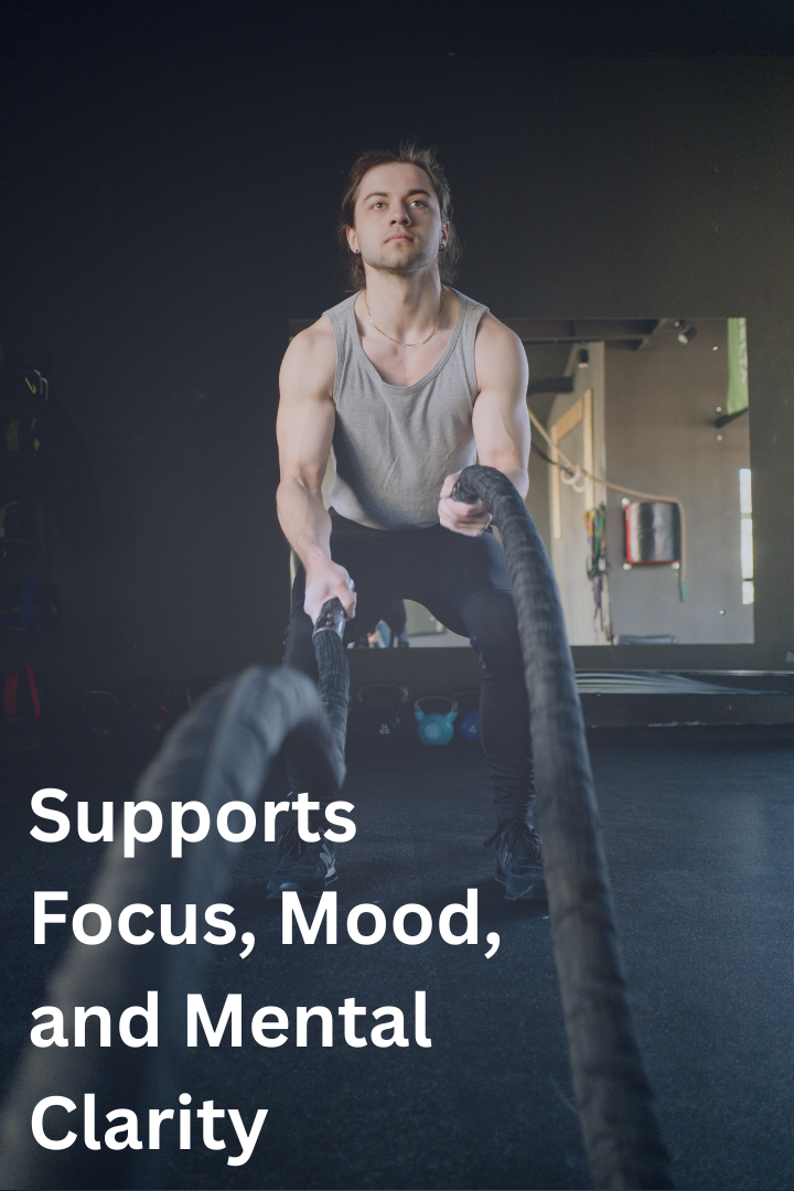 A man in a gym performing a battle rope exercise with a focused expression. The gym has weights and equipment in the background.