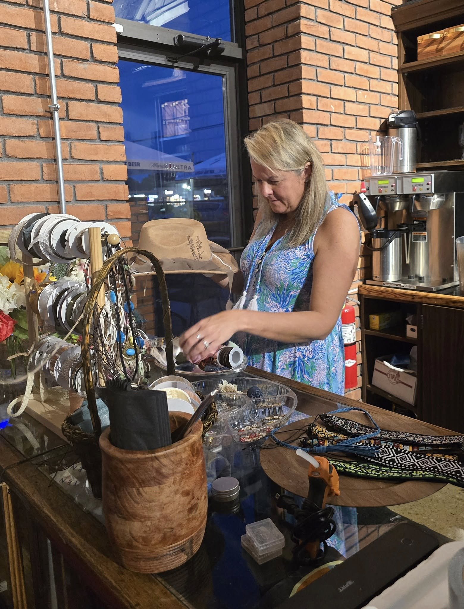 A woman with blonde hair wearing a blue patterned dress choosing embellishments for her custom burnt hat.