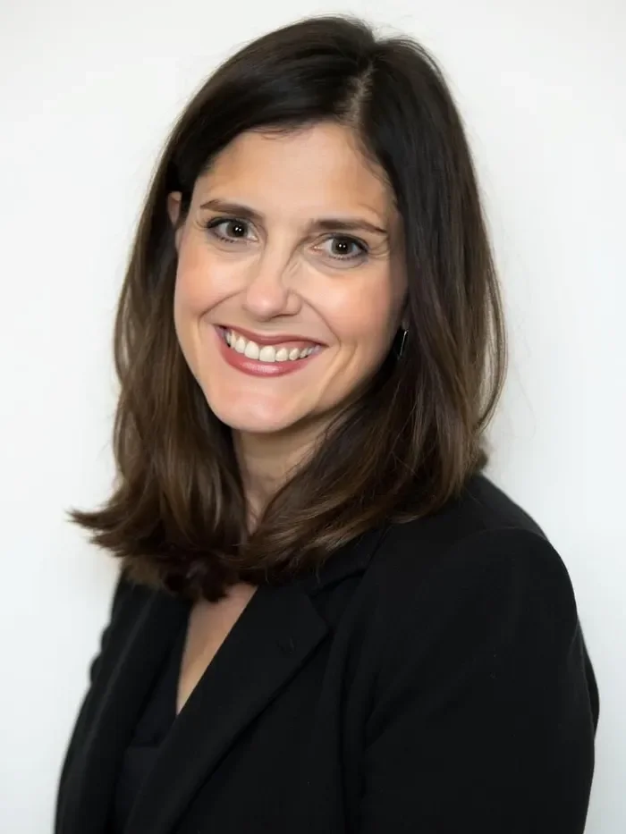 A woman with shoulder-length brown hair and a black blazer smiling at the camera.
