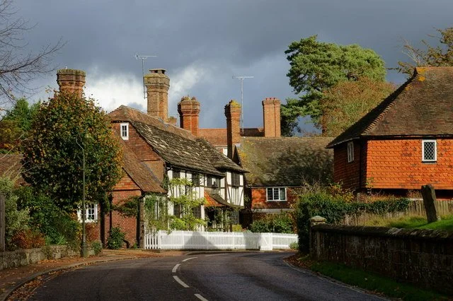 Charming village street with traditional brick and timber cottages, a winding road, and overcast sky