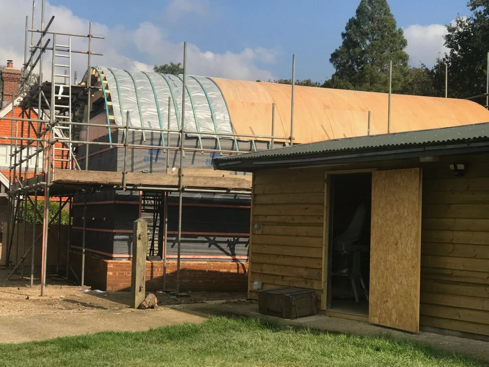 Construction site with a building under renovation, scaffolding surrounding the structure, and a small wooden shed nearby.