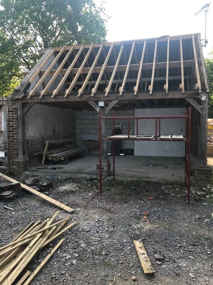 Under construction backyard shed showing roof framing, construction scaffolding, and building materials.