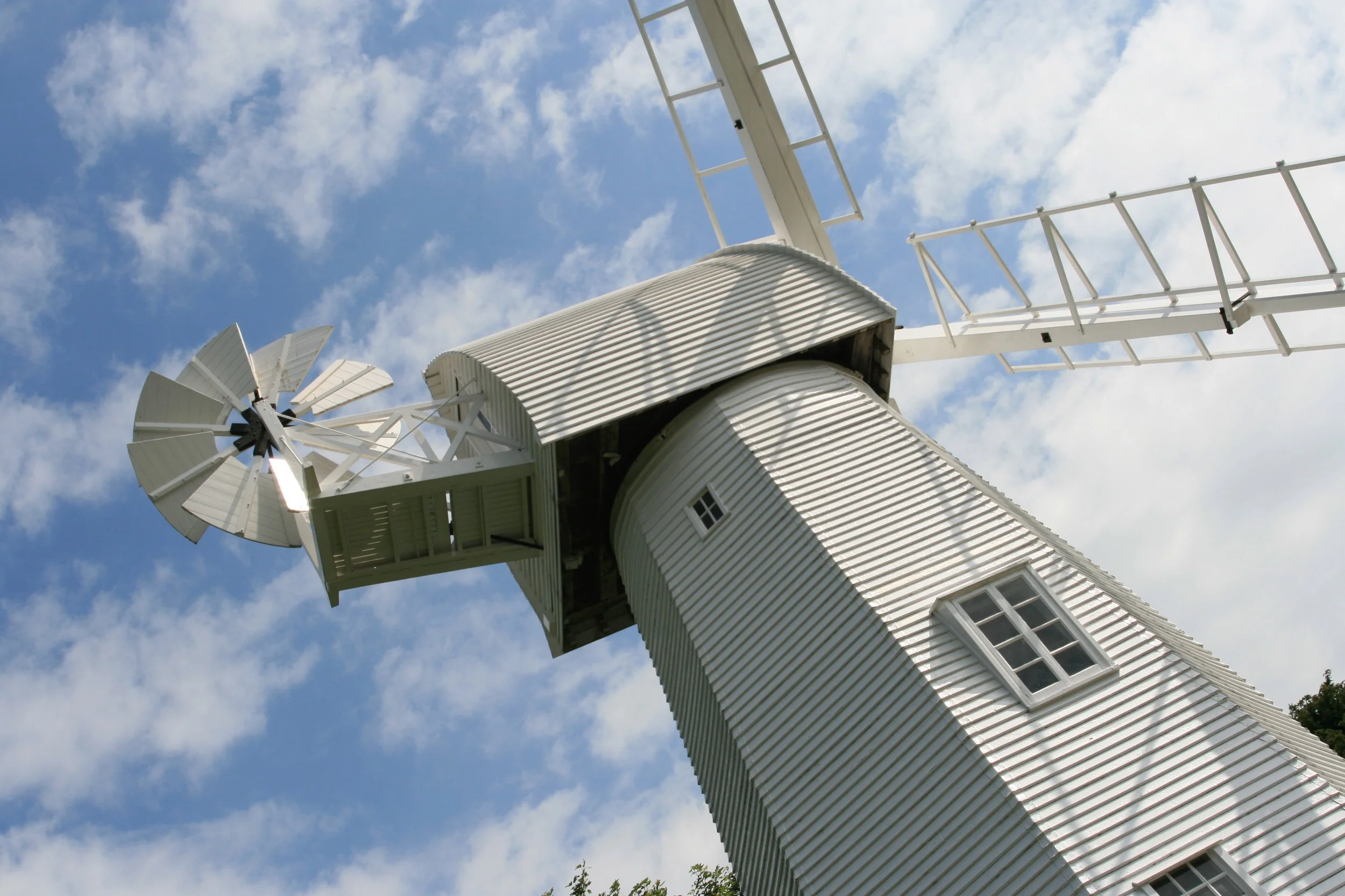 A windmill with white blades and a white tower against a blue sky with scattered clouds.