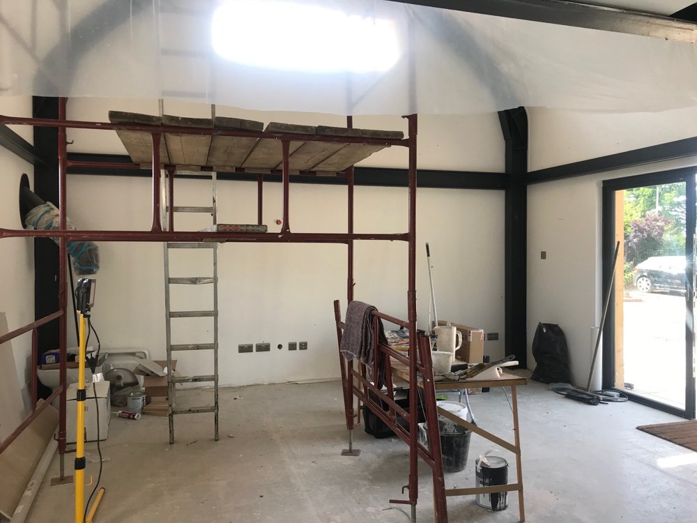 Interior of a room under construction with scaffolding, ladder, construction tools, and materials scattered around.