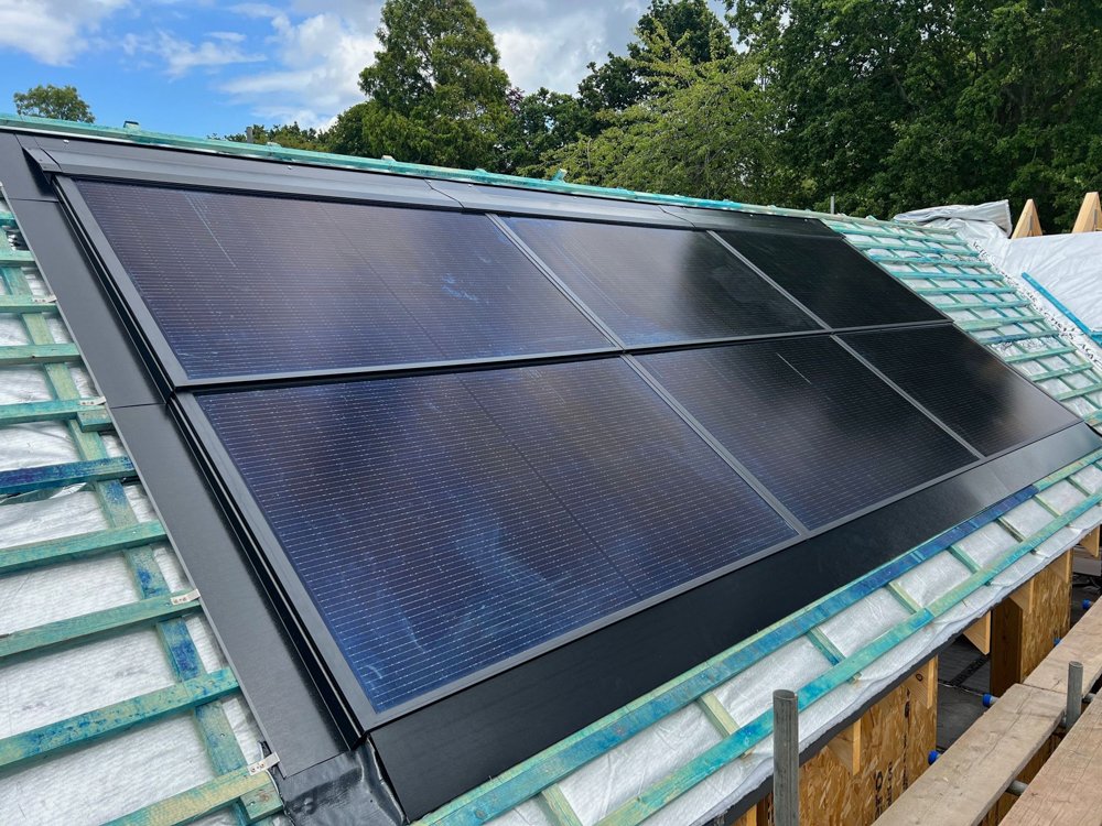 Solar panels installed on a house roof during daytime with a background of green trees and partly cloudy sky.