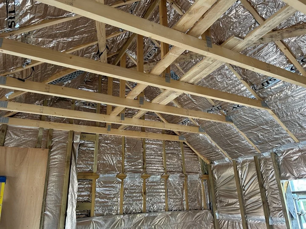 Interior of a house under construction with wooden framing and insulation on the walls and ceiling.