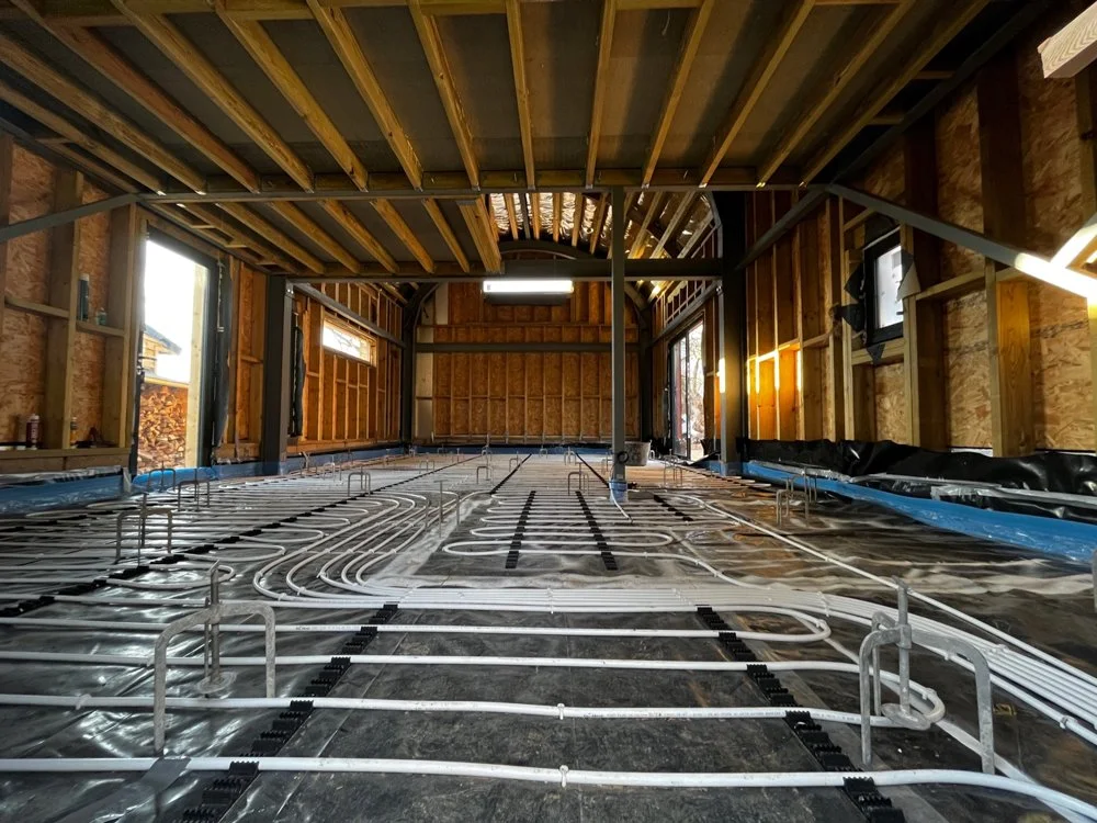 Interior of a building under construction with visible electrical and plumbing ductwork, wooden framing, and exposed ceiling beams.