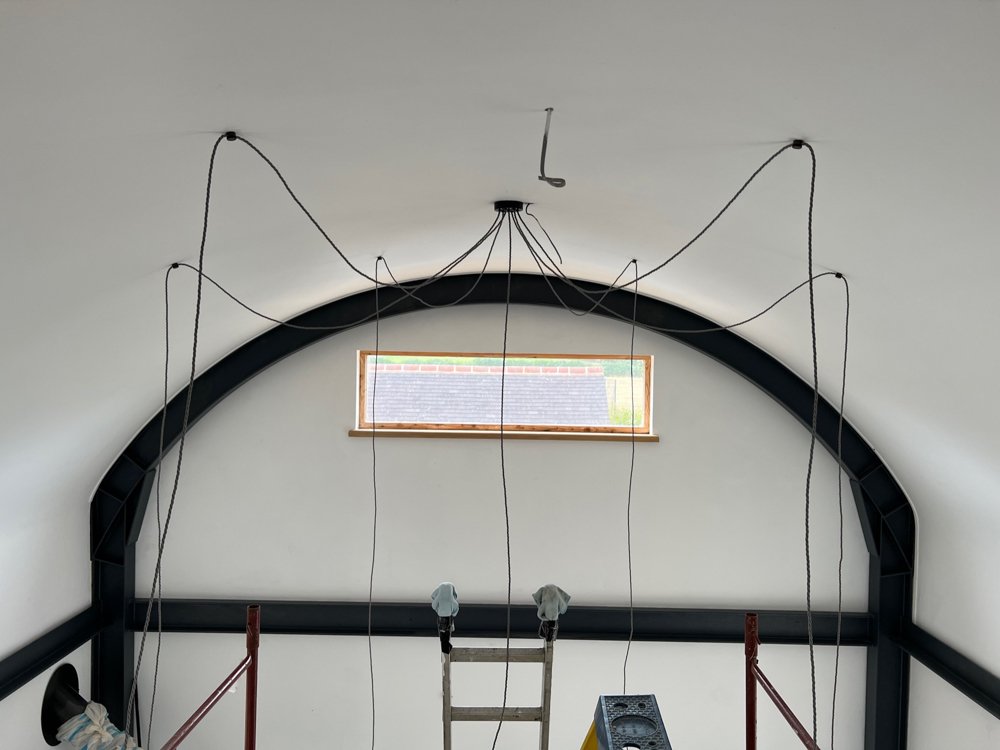 Interior of a building under construction with a high vaulted ceiling, black steel arch, small horizontal window, and scaffolding.