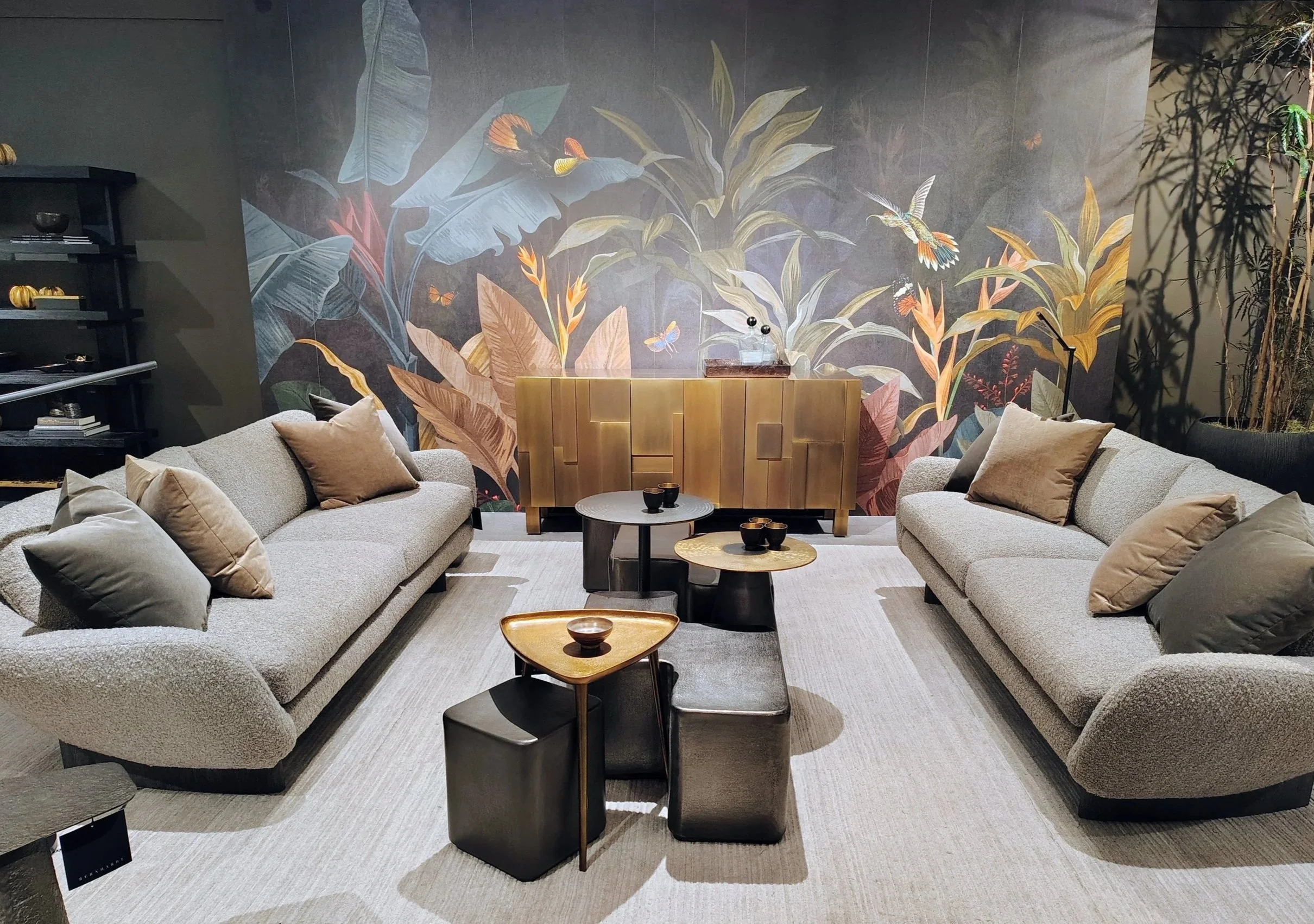 Living room with two beige sofas, black and gold nesting tables, and a large wall mural of colorful birds and tropical plants.