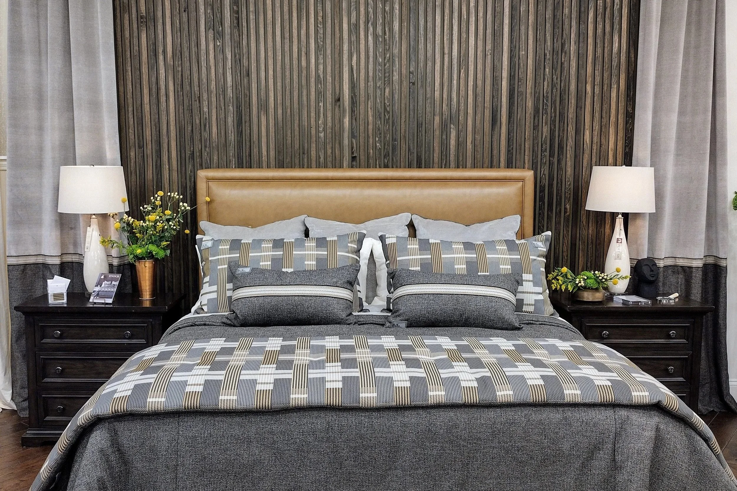 A neatly made bed with patterned bedding, two pillows, and two nightstands with lamps and decorative items, against a wooden paneled wall.