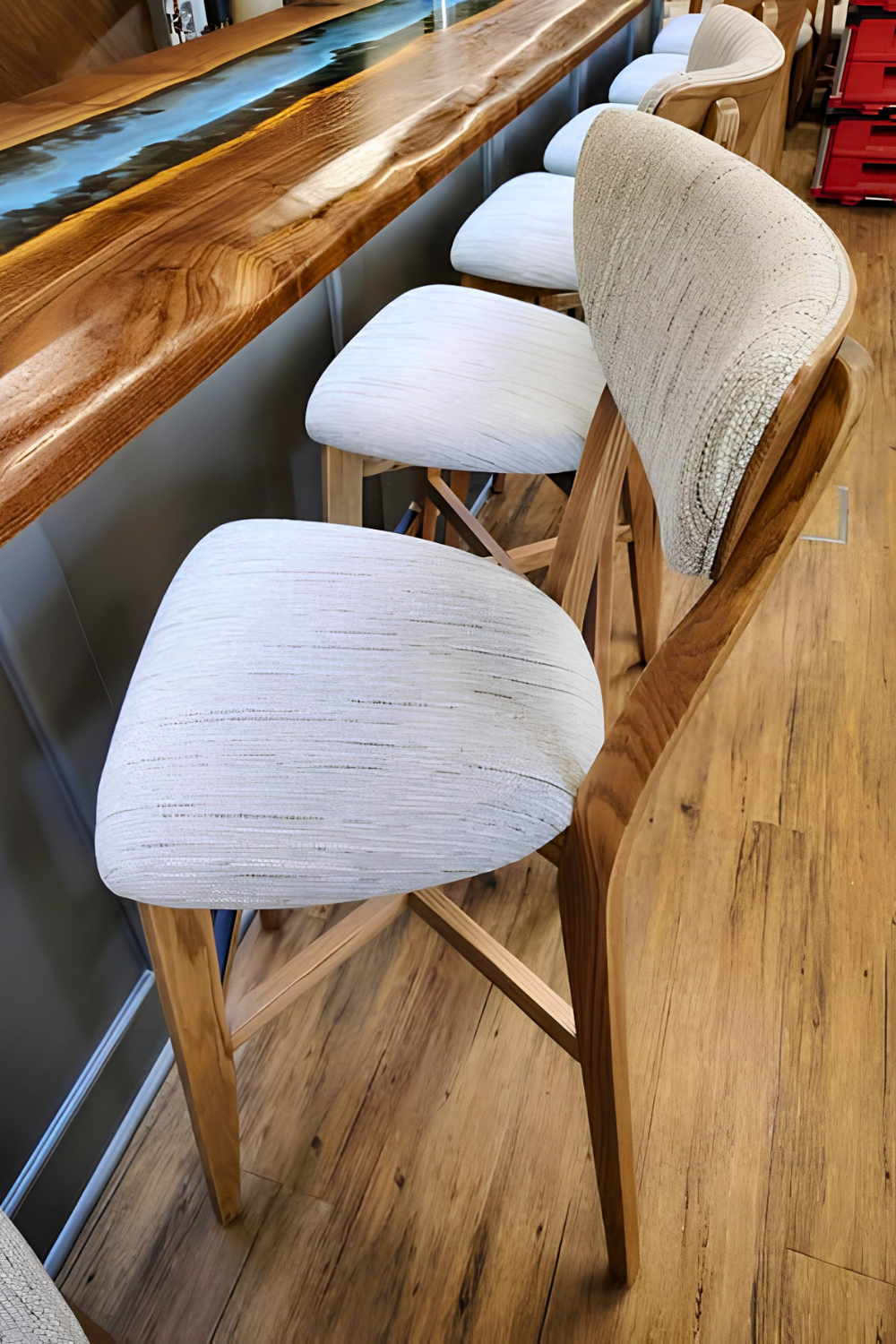 Wooden bar counter with white upholstered bar stools featuring wooden legs.