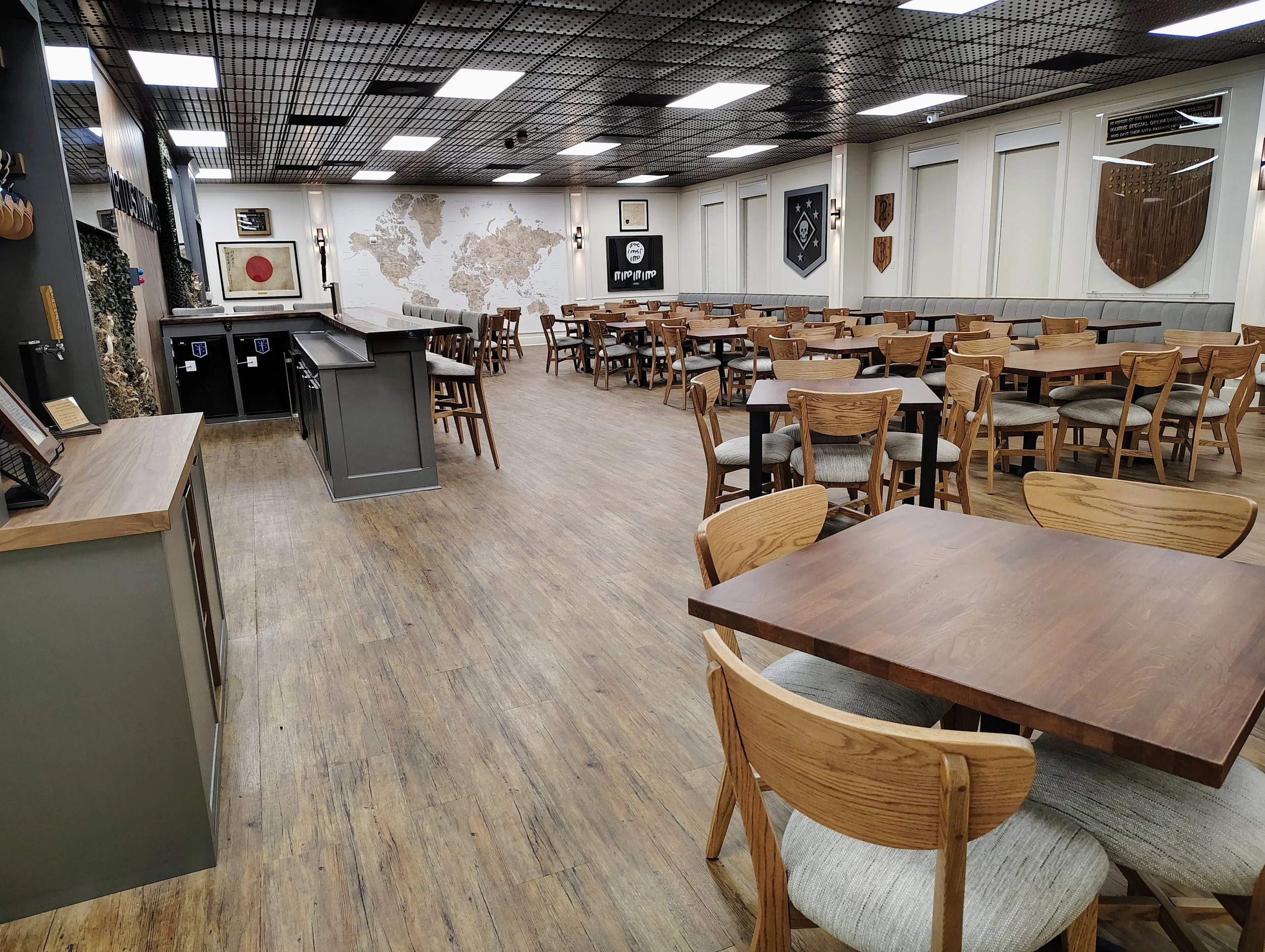 An empty modern restaurant with wooden tables and chairs, a world map on the wall, framed art, and shield-shaped wall decorations.