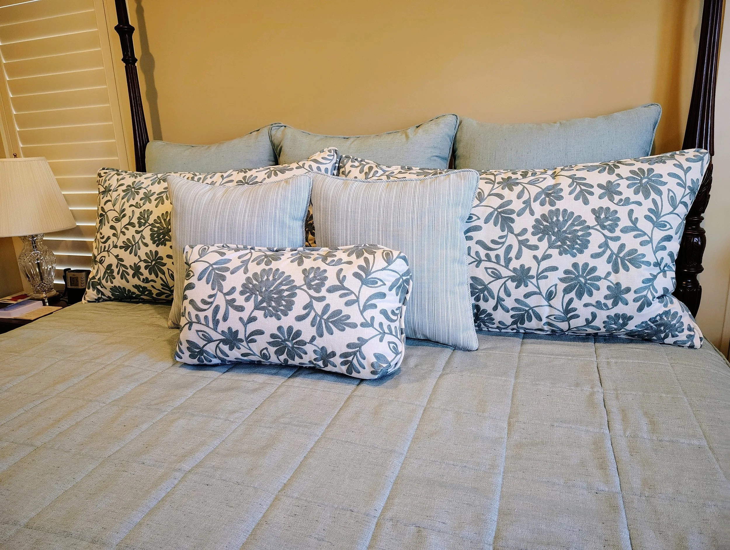 Bed with blue and white floral pillows, striped accent pillows, and a beige quilted bedspread