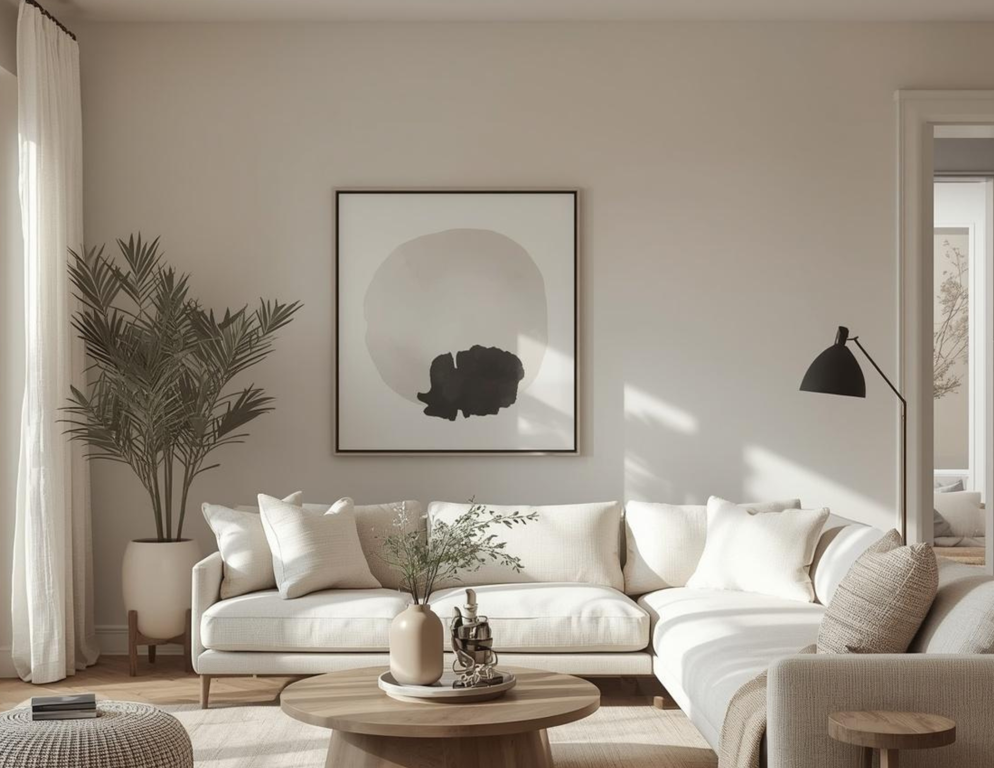 A cozy living room with a large white sectional and netural accessories from wall art to an ottoman.