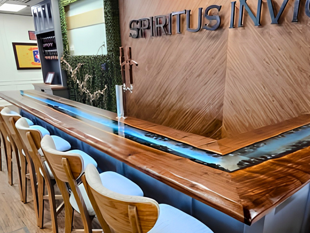 Modern circular bar with water feature, surrounded by wooden chairs, in a stylish interior with the words 'SPIRITU'S IN' on a wooden wall.