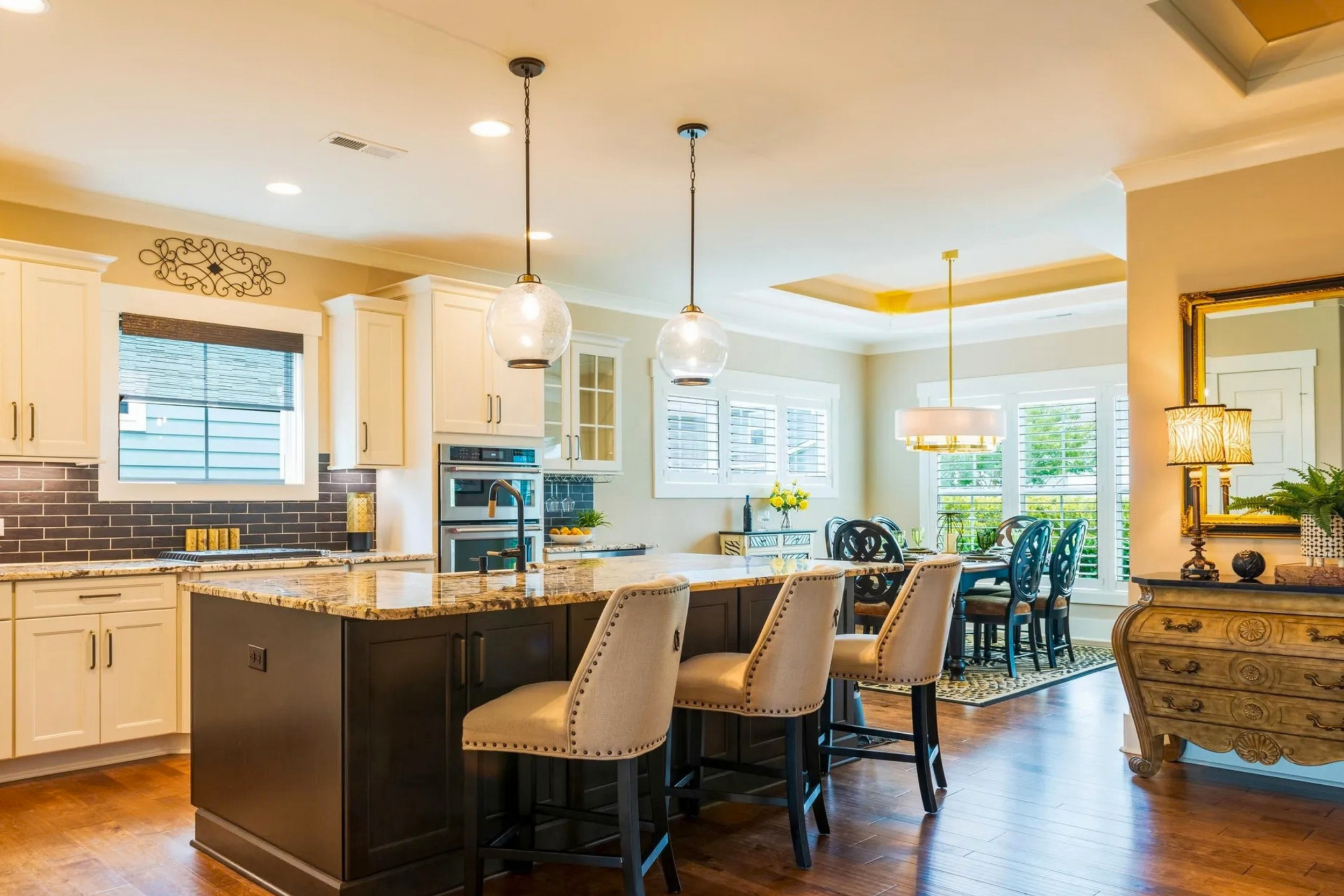 Open-concept kitchen and dining area with white cabinets, a large island with dark base, pendant lighting, and a dining table with chairs near windows.