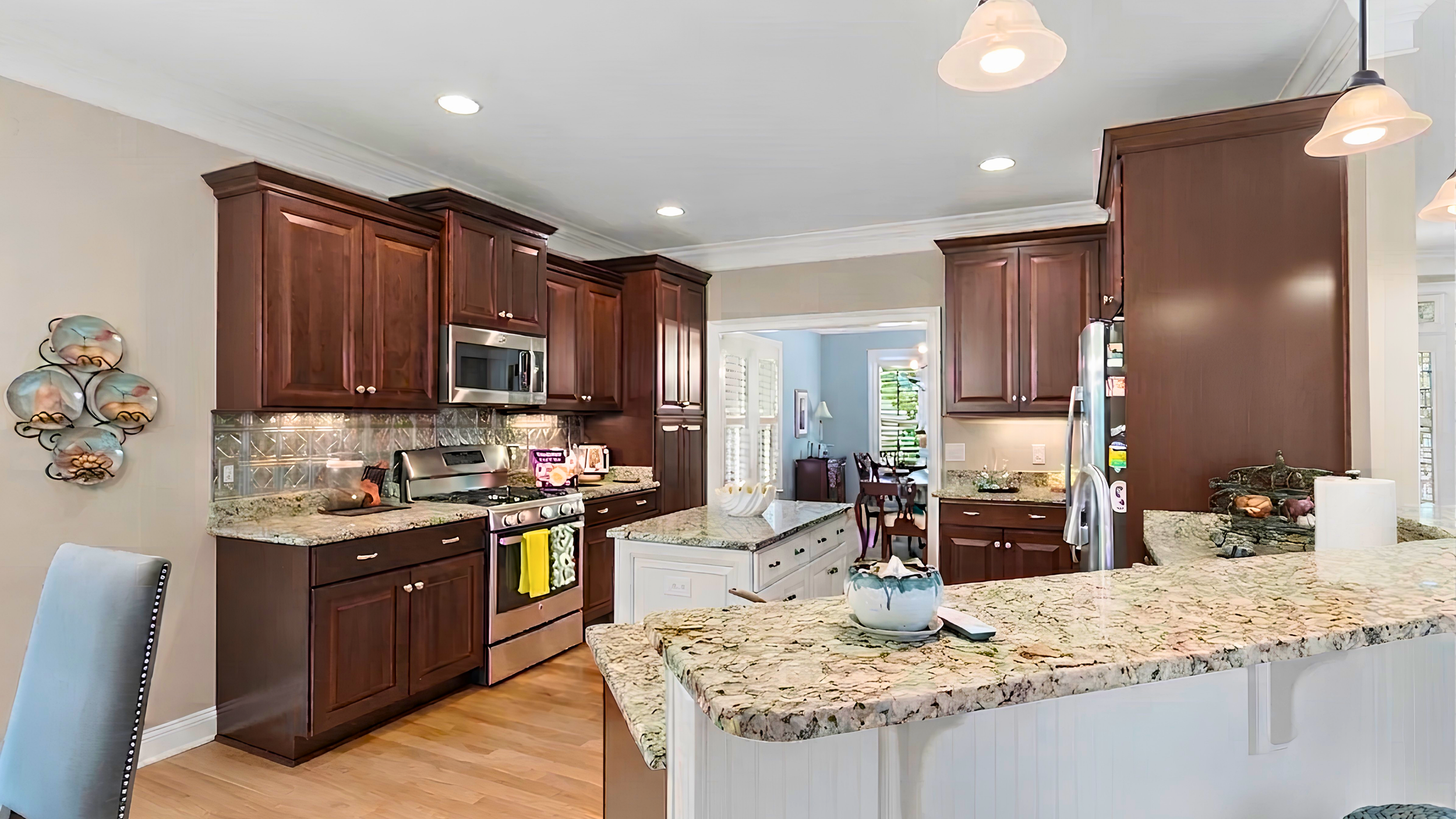Kitchen features dark wooden cabinets, granite countertops, stainless steel appliances, a kitchen island with a white base, and a dining area visible in the background.