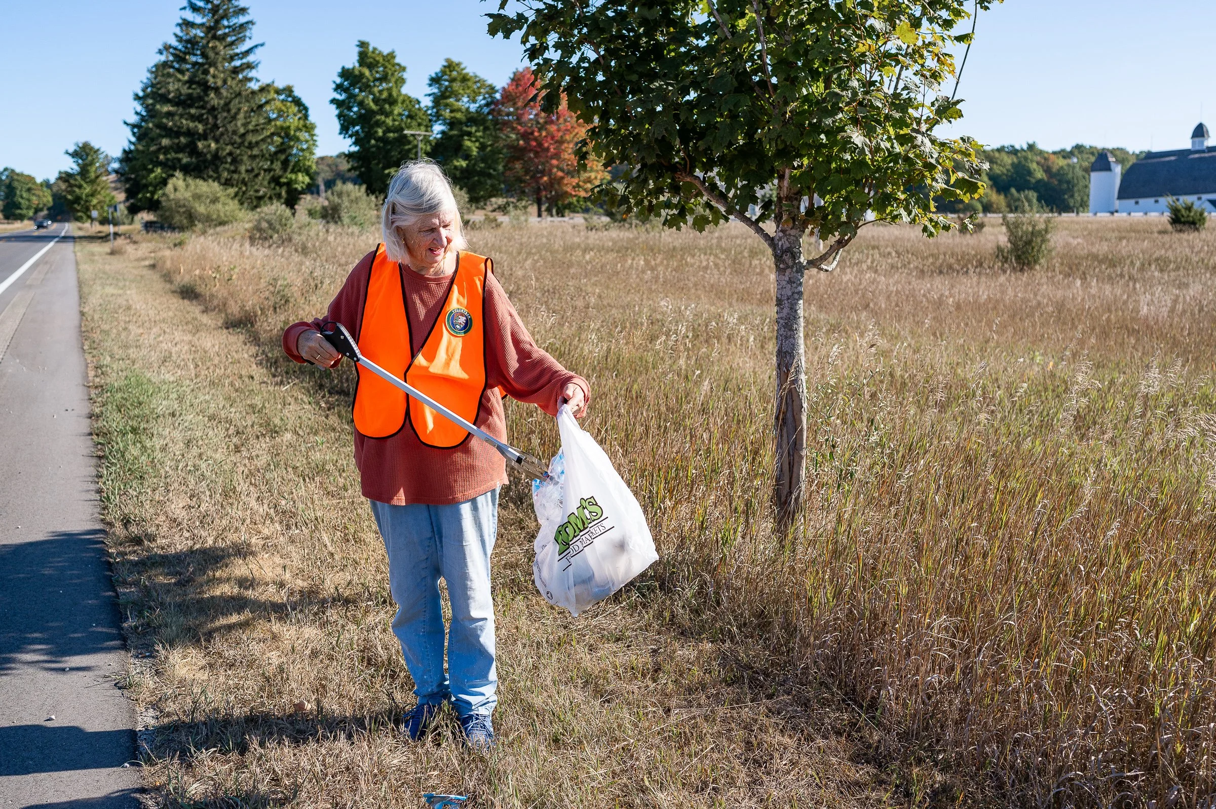 adopt a highway volunteer in orange vest picking up litter on the side of a highway