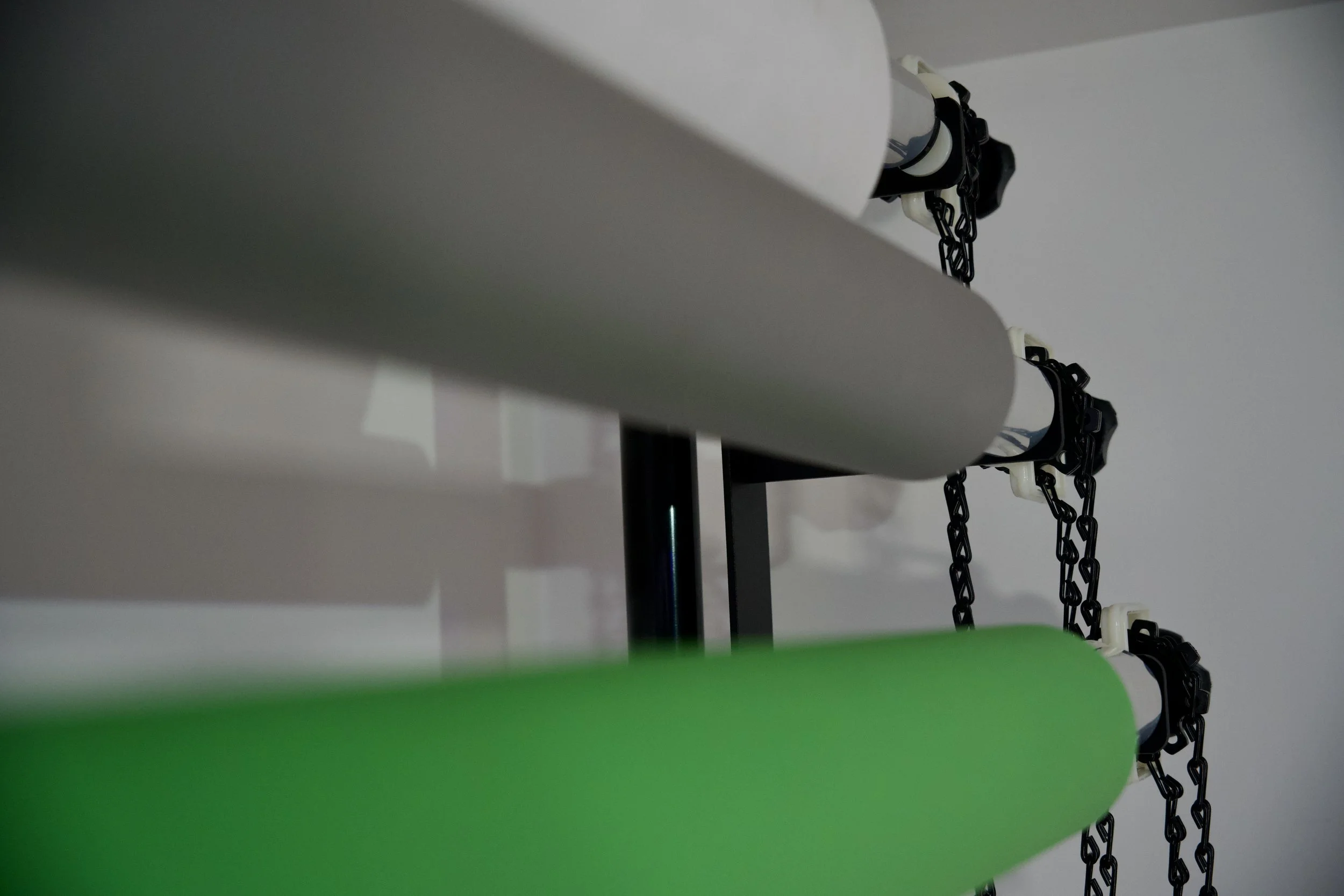Close-up view of two cylindrical foam rollers, one white and one green, mounted on a black stand with black chains hanging down.