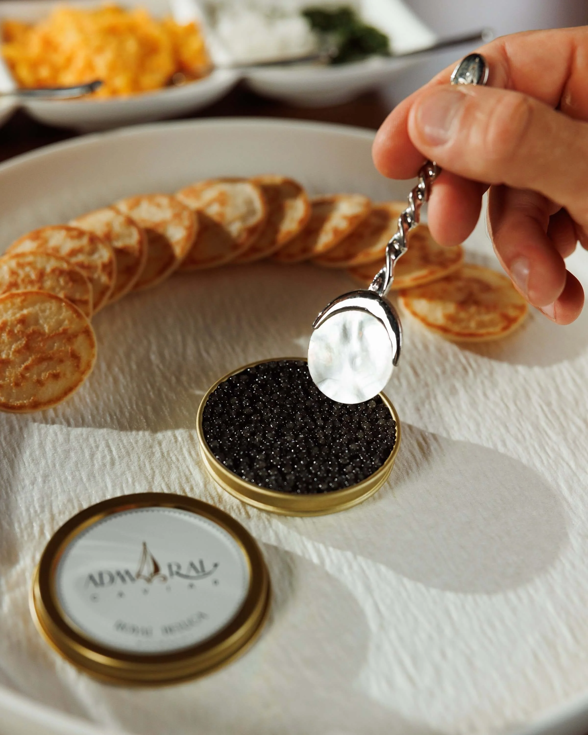 Mother-of-pearl and metal caviar spoon held over a tin of Admiral caviar