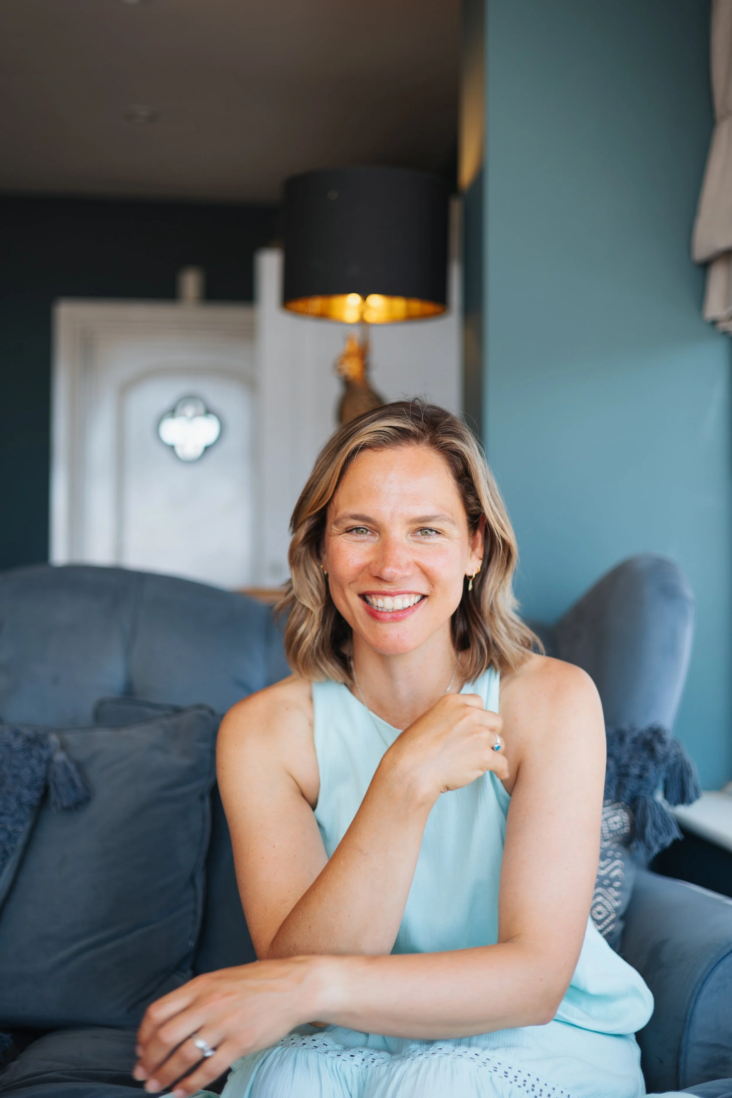 Louise with short blonde hair smiling and sitting on a blue sofa in a living room.