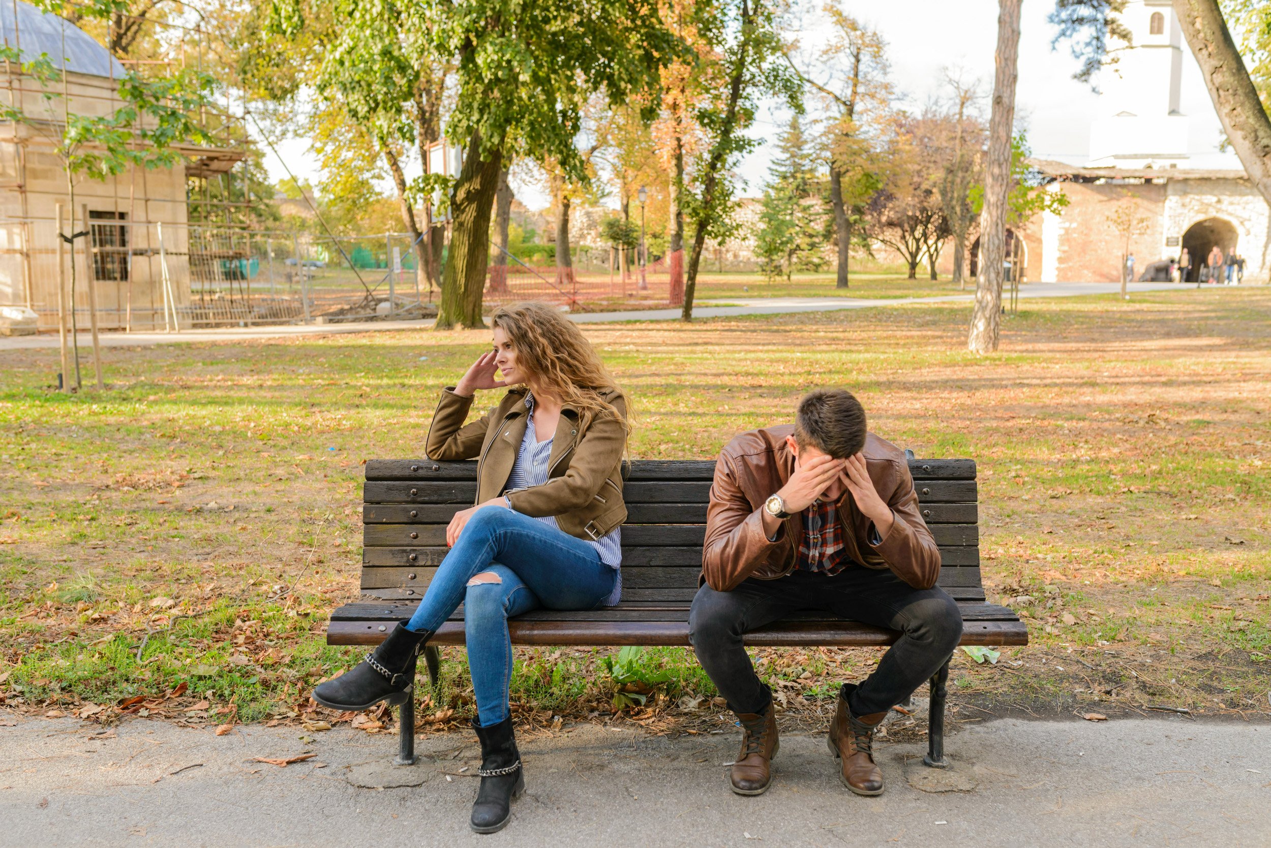 partners sit on a bench outdoors, struggling to communicate effectively