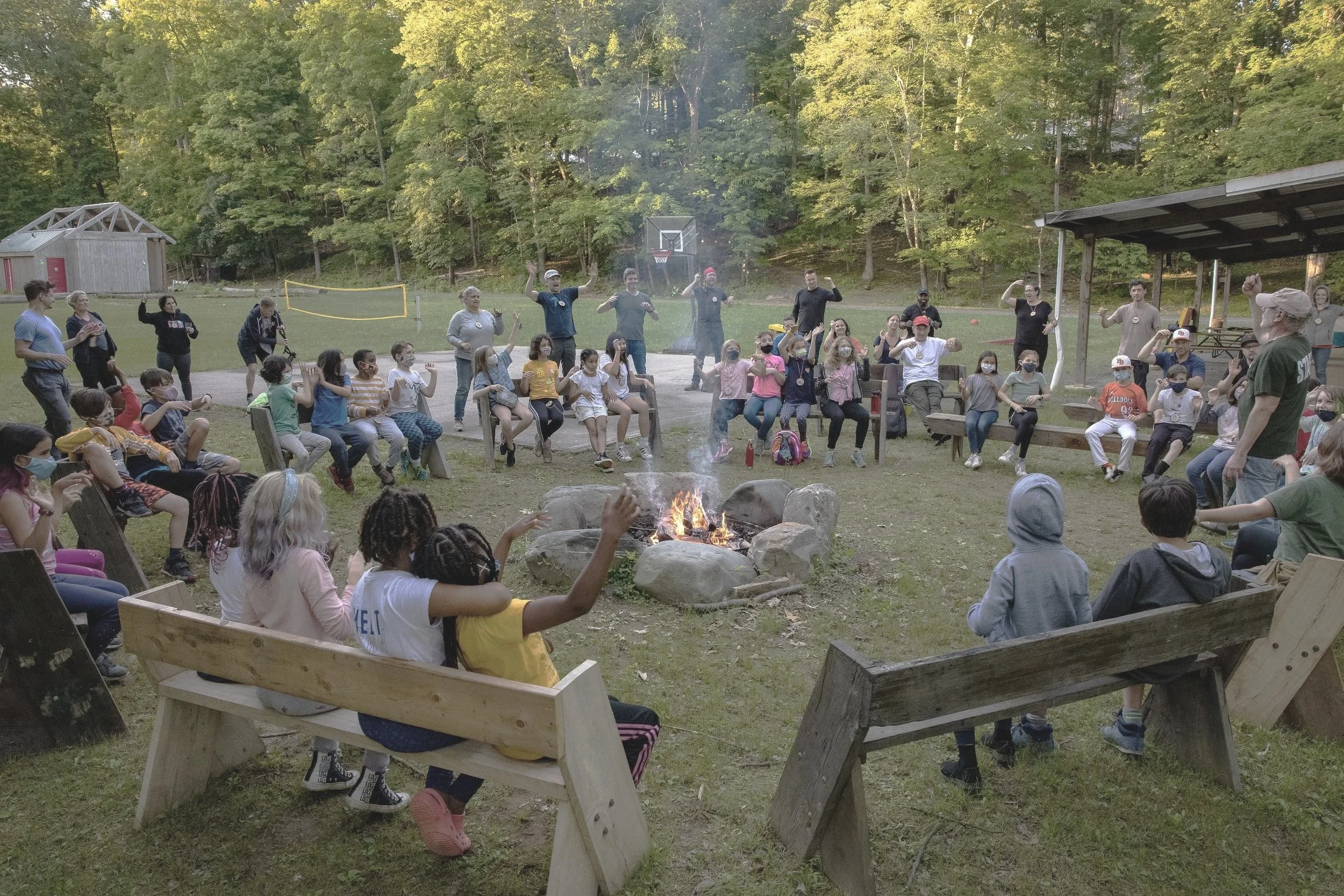A group of children and adults dance and sing around a campfire at the Ashokan Center during the Ashokan Music & Dance Camps.