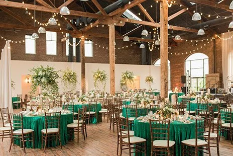 Refinery South wedding venue with round tables covered in teal tablecloths and chivari chairs, inside a brick building with high ceilings.