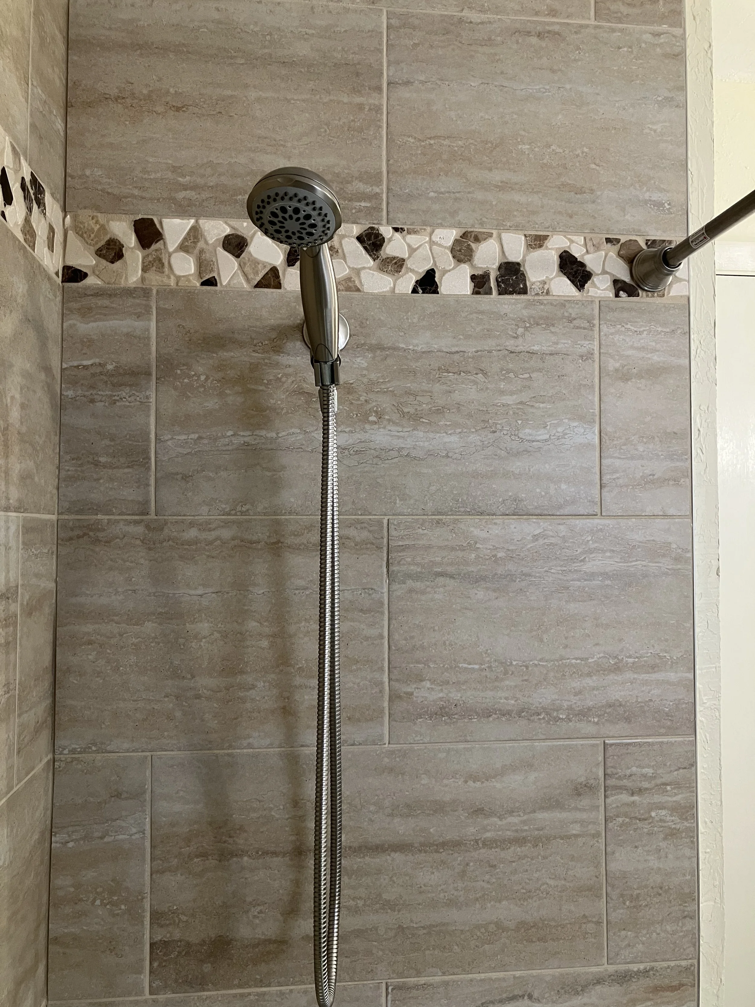 Close-up of a showerhead with a flexible hose in a tiled shower.