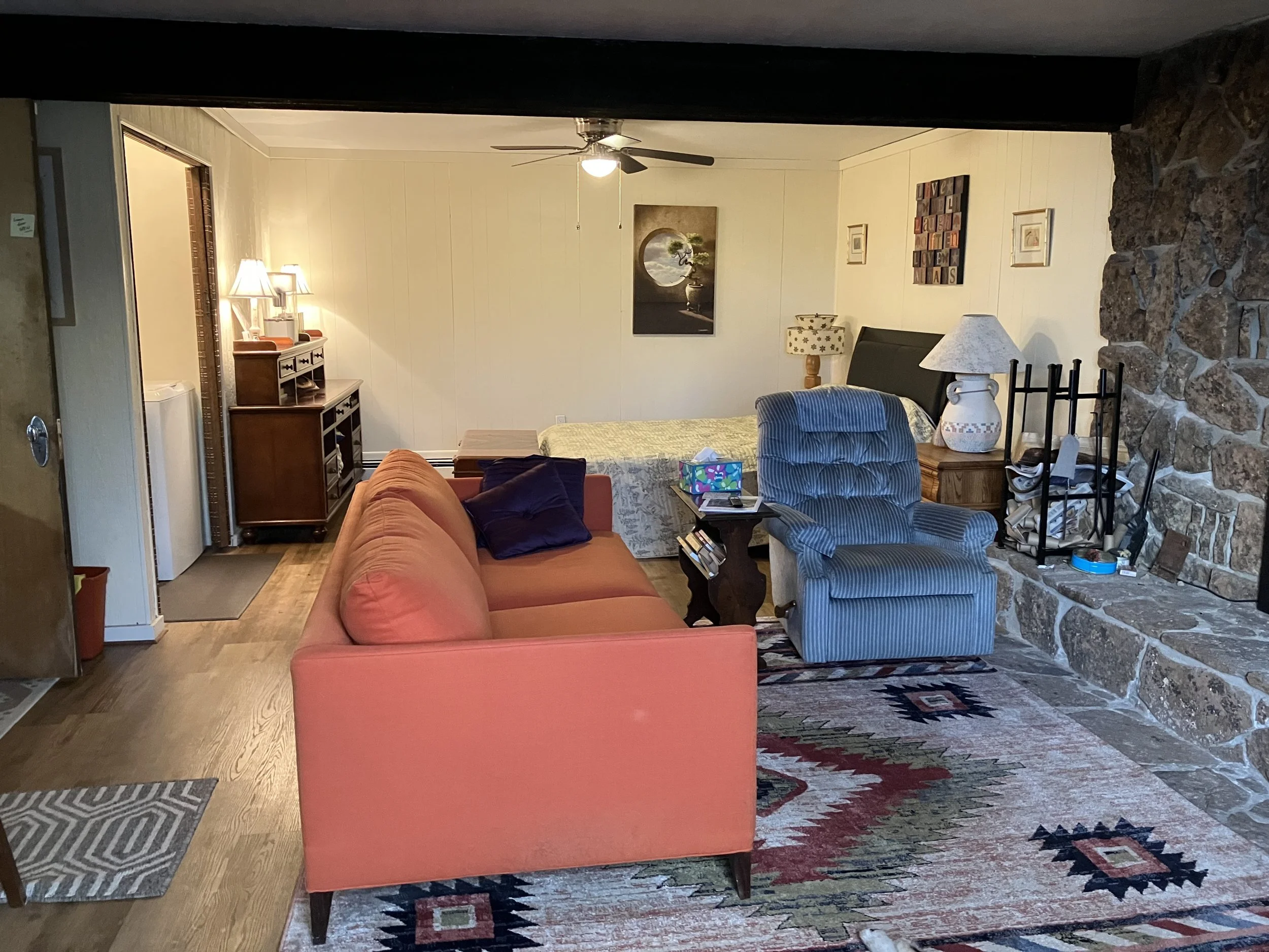 Living room with a coral sofa, striped armchair, stone fireplace, wooden furniture, lamps, and artwork on the walls.
