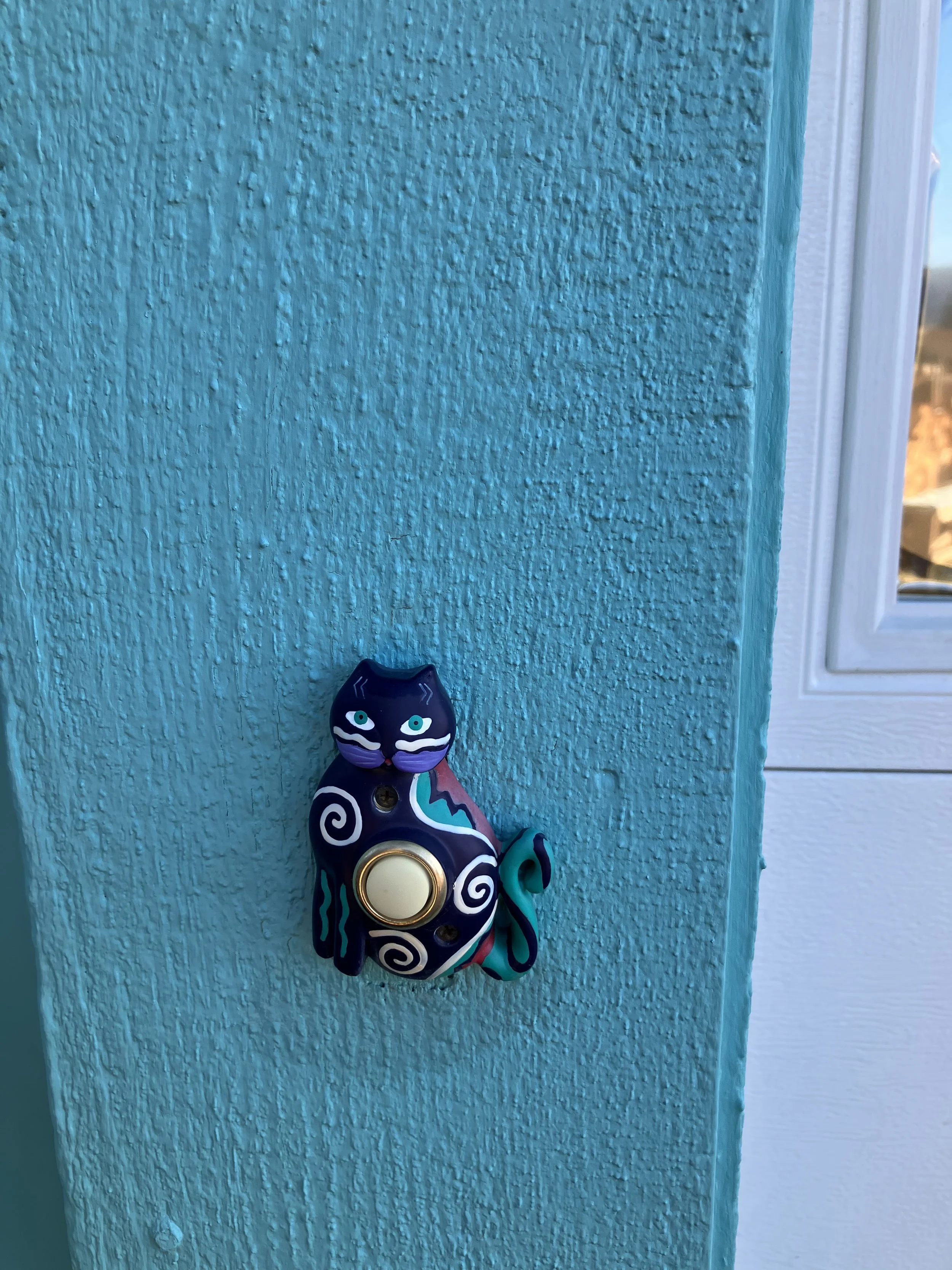 Decorative cat-shaped doorbell on a textured turquoise wall.
