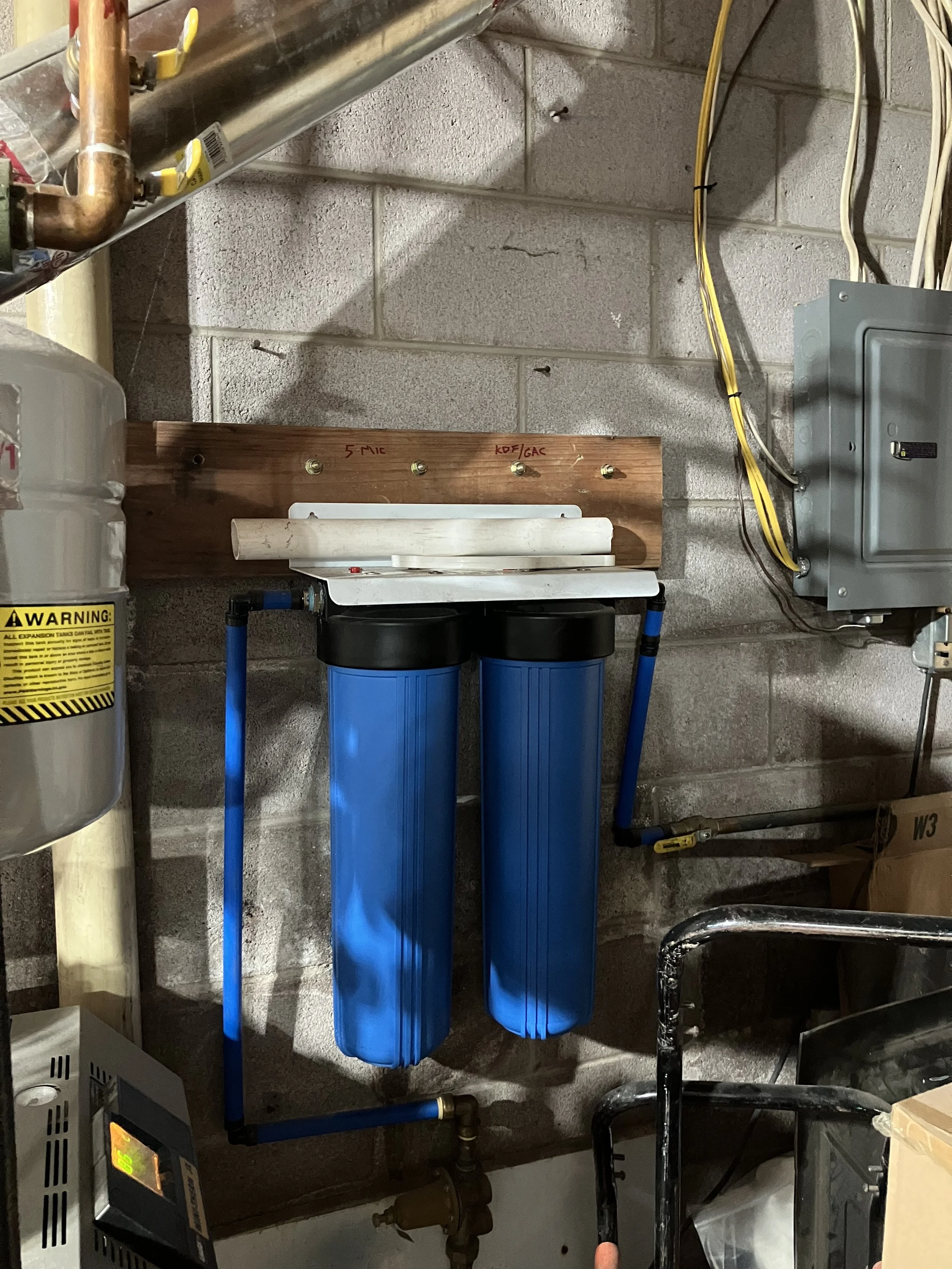 Water filtration system with two blue filtration units mounted on a brick wall in a utility room.