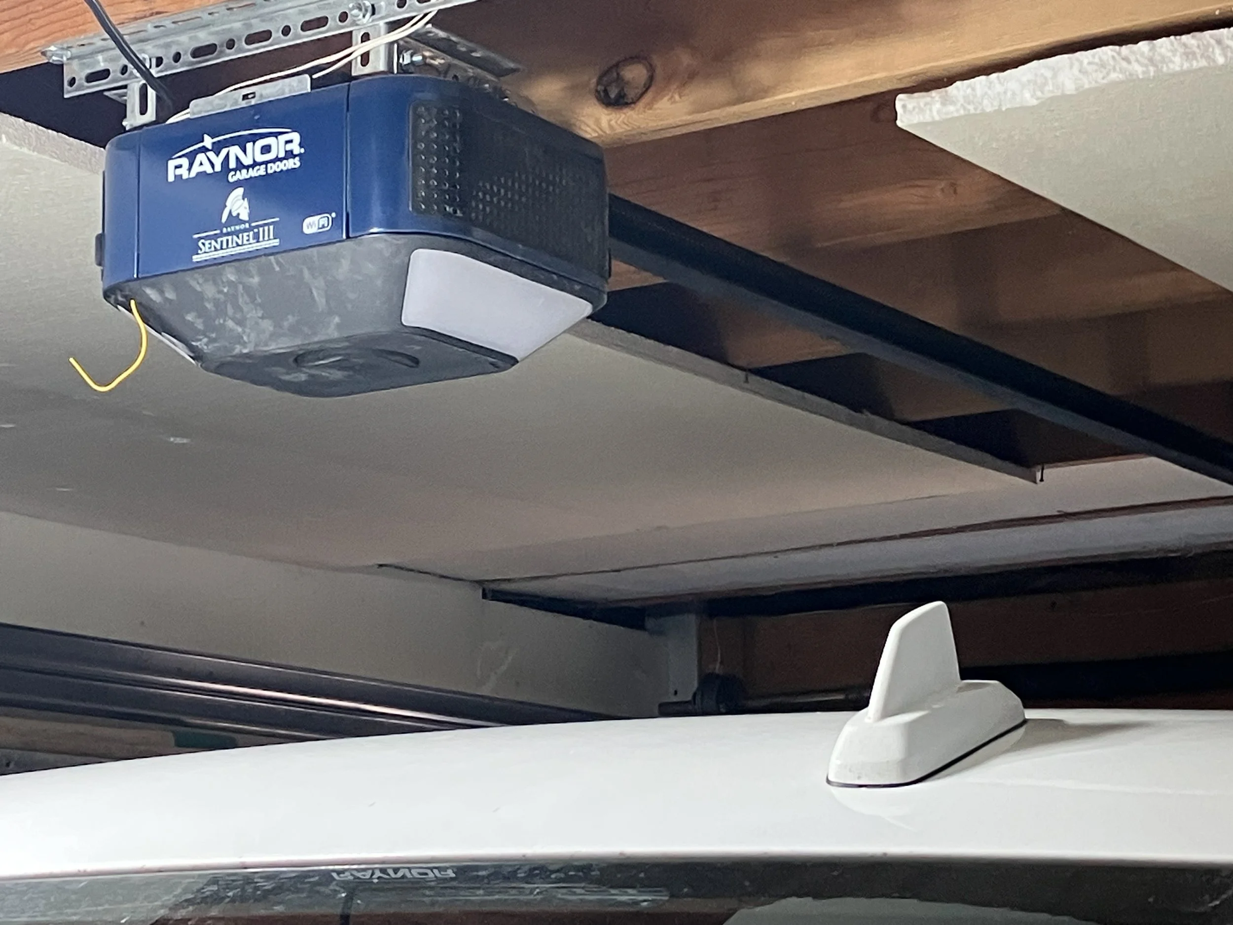 Garage ceiling with a Raynor garage door opener and a white antenna attached to the top of a white vehicle.