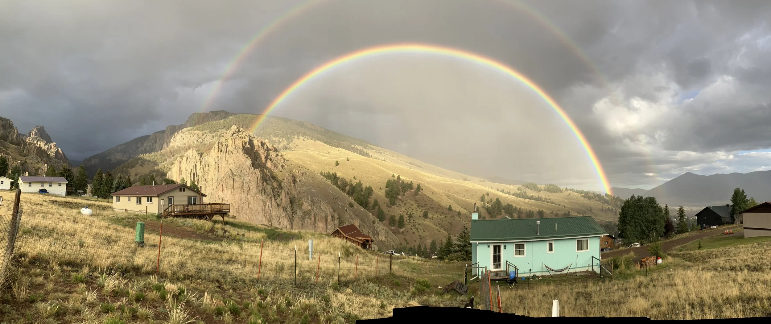 A landscape with a double rainbow over a mountainous area, with several houses and grassy fields in the foreground.
