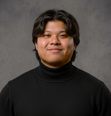 Portrait of a young man with dark hair, wearing a black turtleneck sweater, smiling against a gray background.