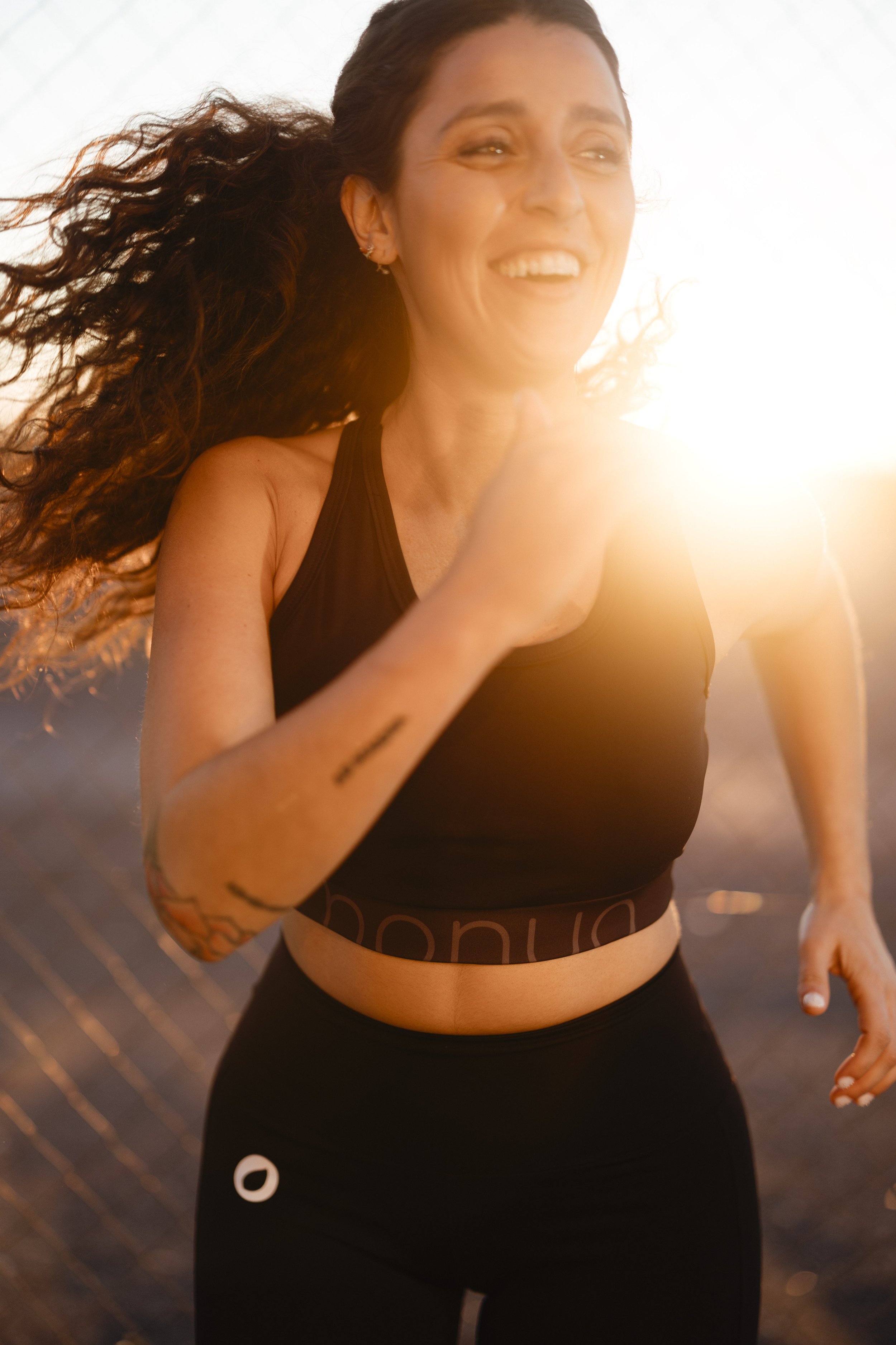 Mujer corriendo al aire libre al atardecer, con cabello rizado y ropa deportiva negra.