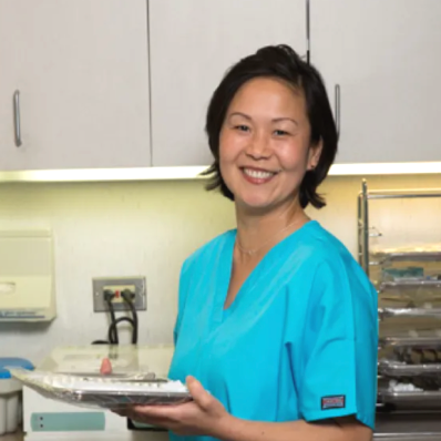 A woman, our teammate Jackie, in blue scrubs smiling in a medical or laboratory setting.
