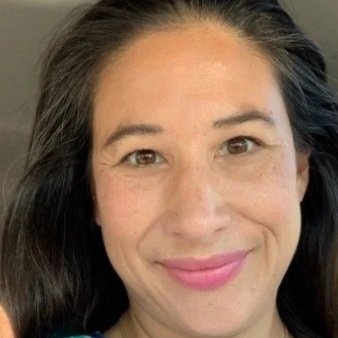 Close-up of a woman with dark hair smiling against a blurred background.