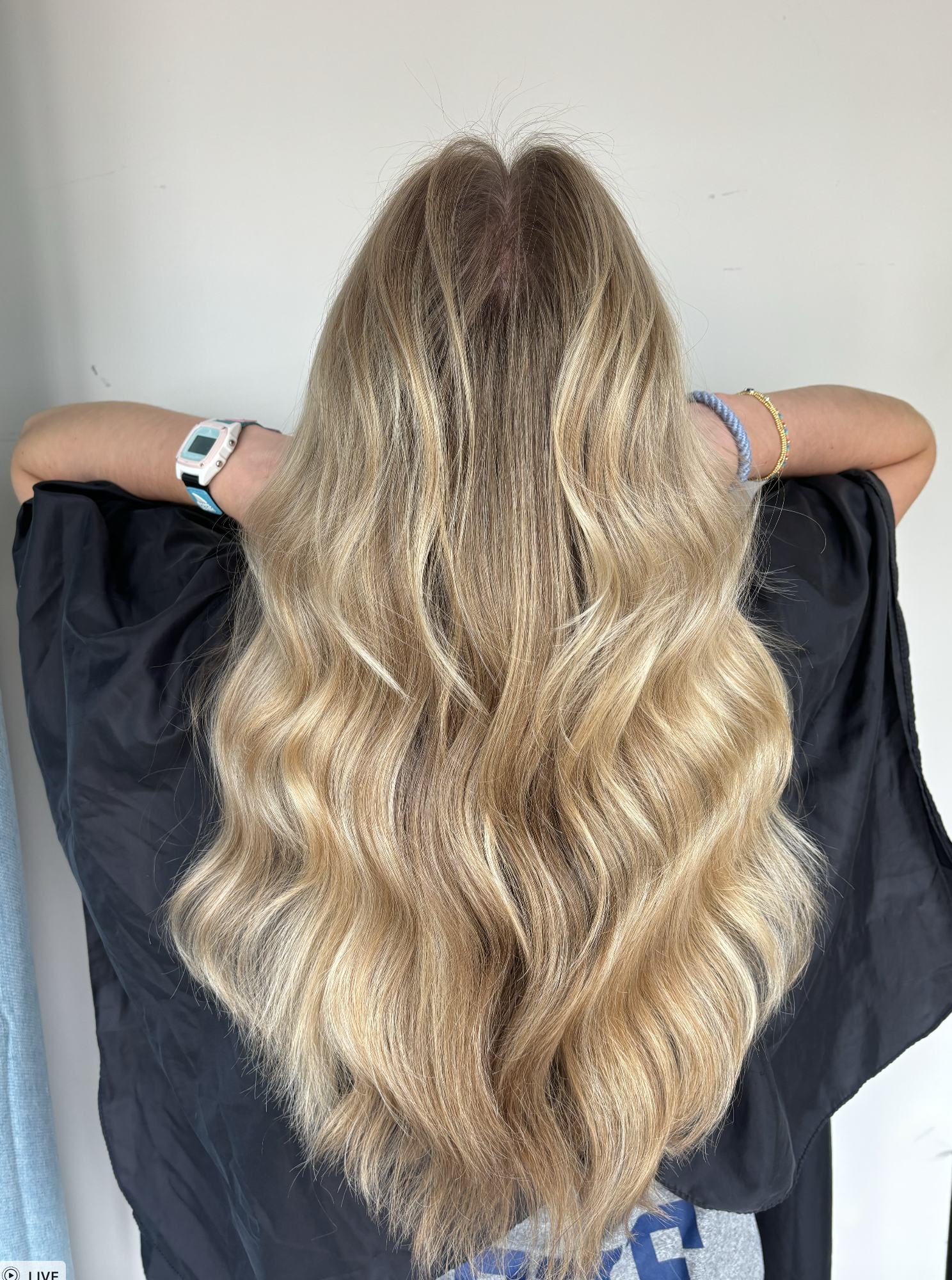 Person with long, wavy blonde hair wearing a black cape, showing the back of their head.