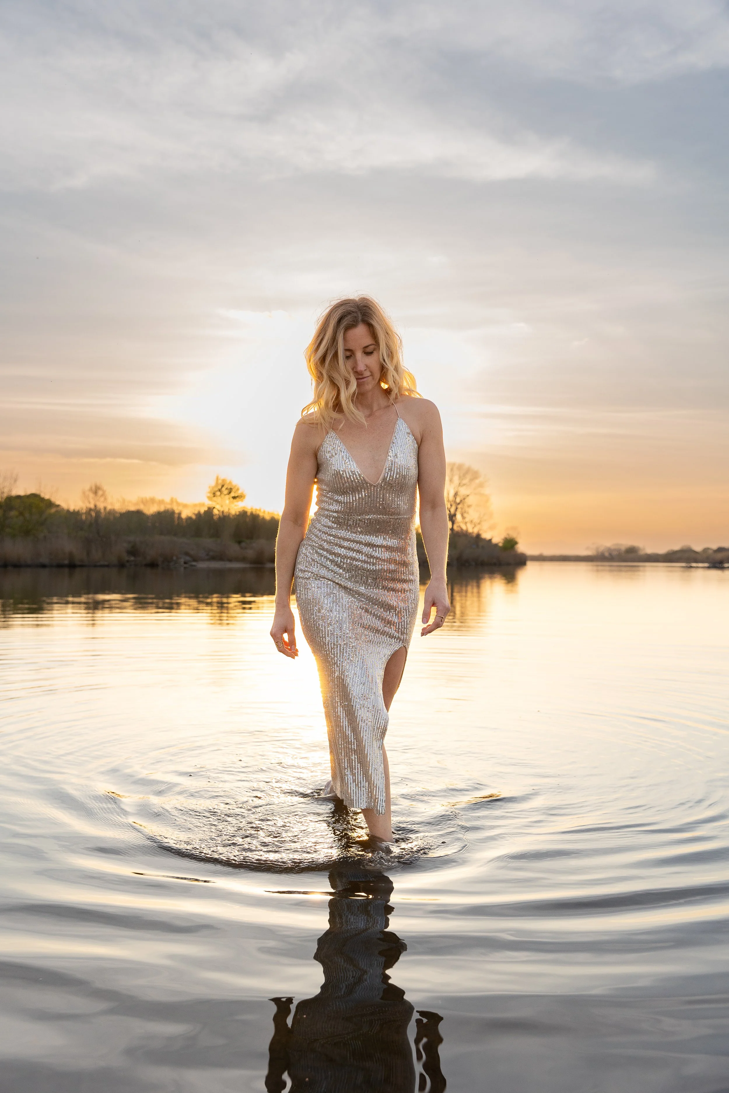 Bee Rose, founder of Inspired by Alchemy, walking through shallow water at sunset in a silver sequin gown